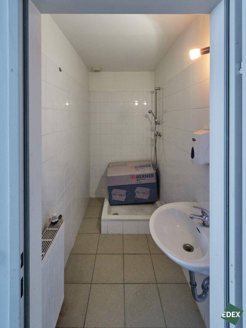 Kleines Badezimmer mit Waschbecken und Duschbereich, komplett gefliest und funktional.