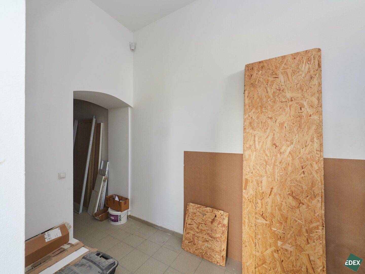 Raum mit weißen Wänden und Holzplatten, die an der Wand lehnen, möglicherweise ein Lagerbereich.