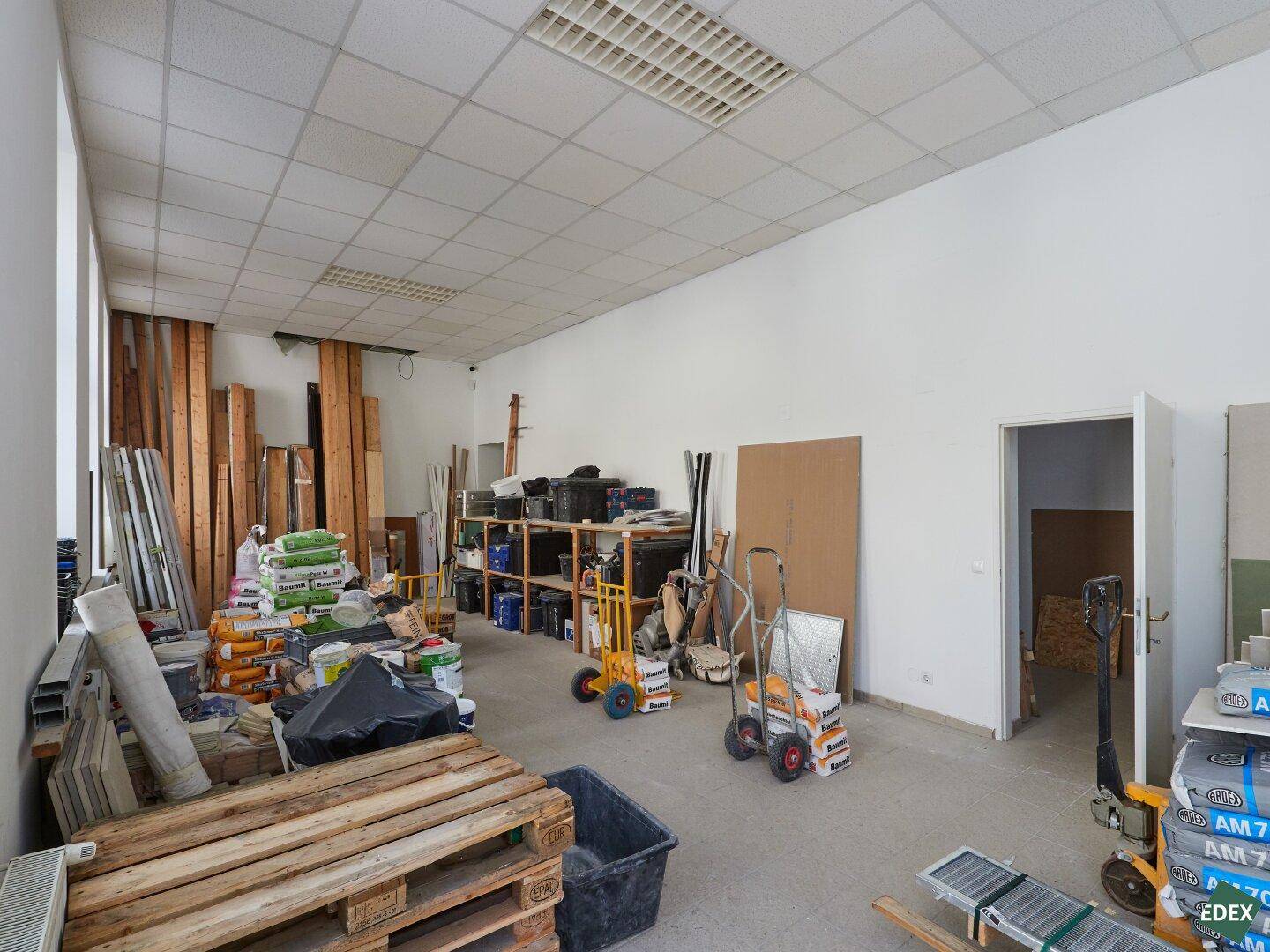 Weiterer Blick in den großen Lagerraum mit Baumaterialien und einem offenen Durchgang.