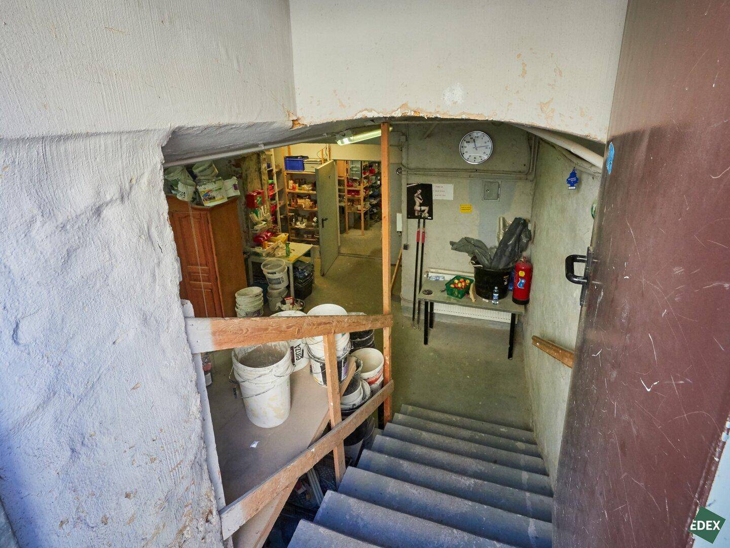 Treppe führt hinunter in einen Kellerbereich, der als Lagerraum mit verschiedenen Eimern dient.