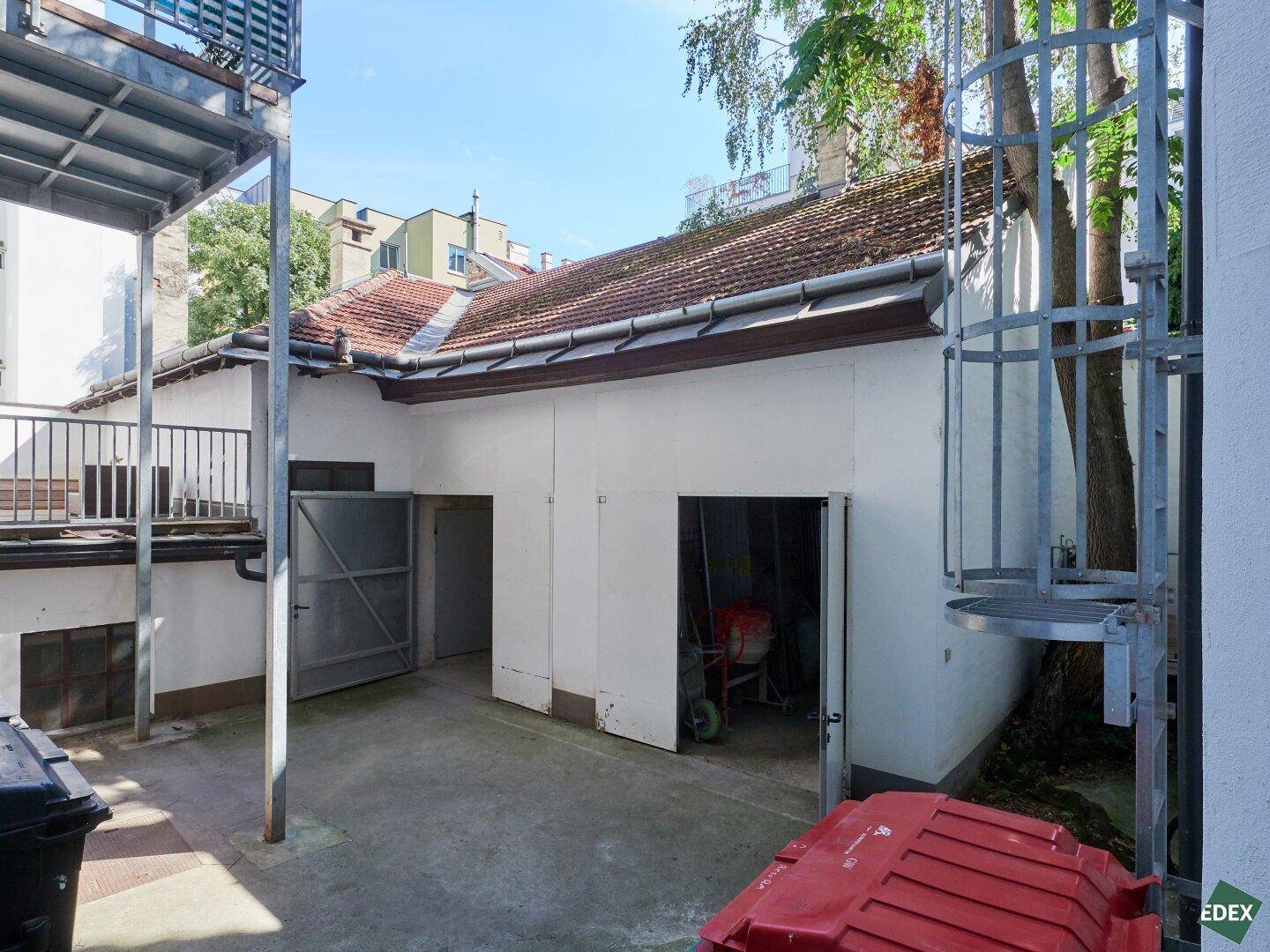 Offene Garagen und Lagerbereiche im Hinterhof, umgeben von alten Gebäuden und Bäumen.