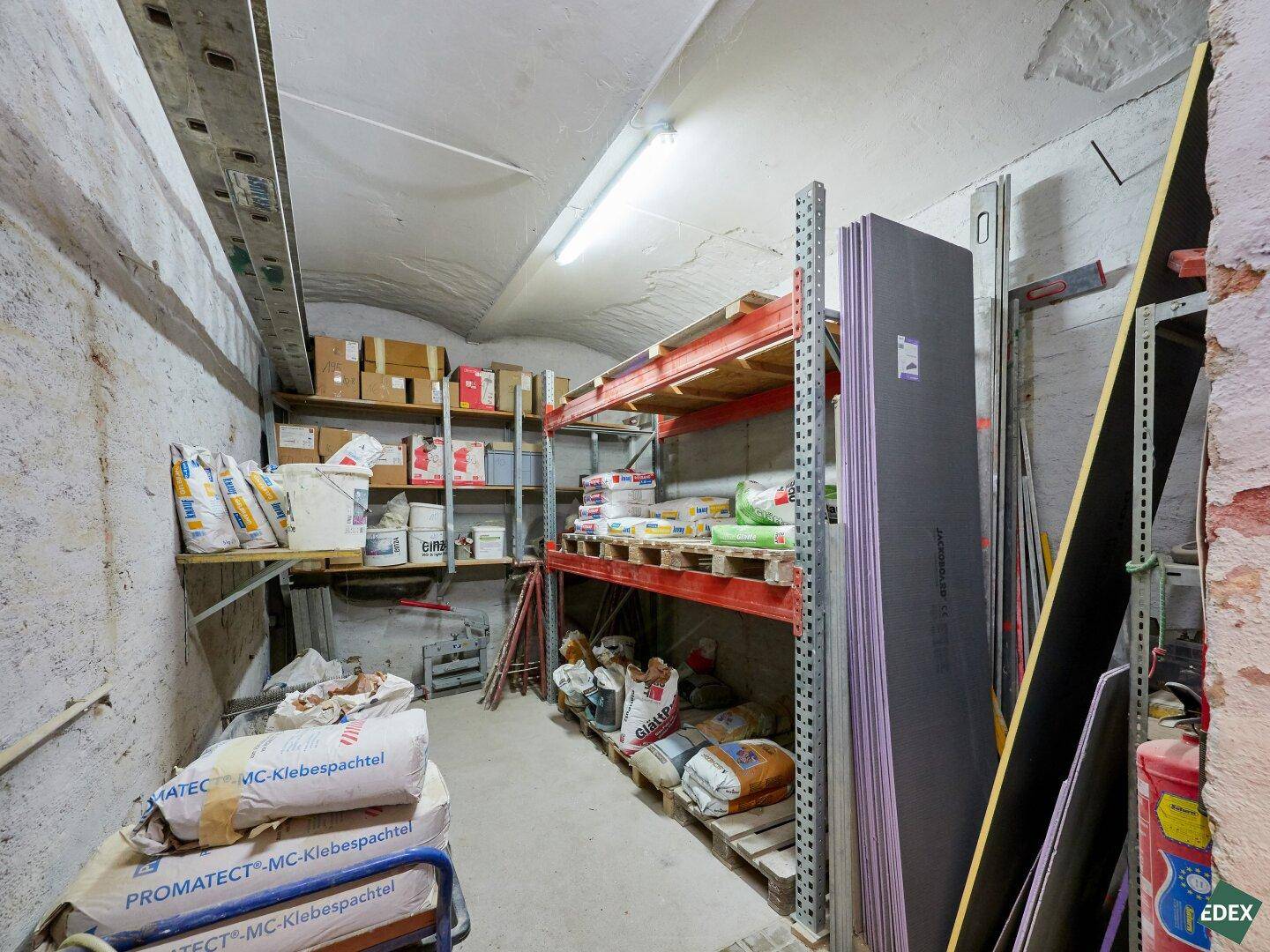 Langer Kellerraum mit Regalen voller Baumaterialien und einer gewölbten Decke.