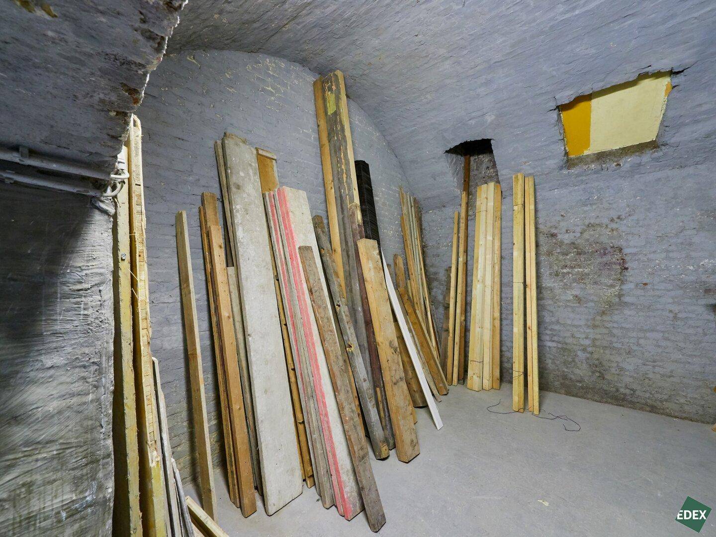 Kellerraum mit Ziegelwänden und gestapelten Holzbrettern, ideal für die Lagerung von Materialien.