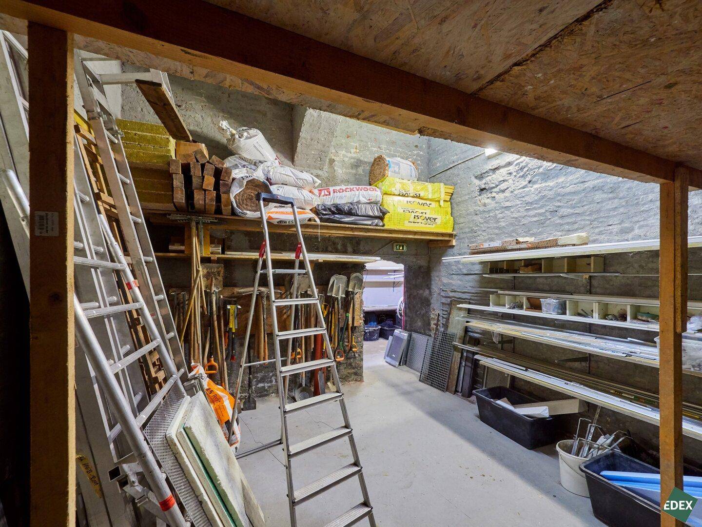 Kellerraum mit Leitern, Regalen und Baumaterialien, unter einer niedrigen Decke gelagert.