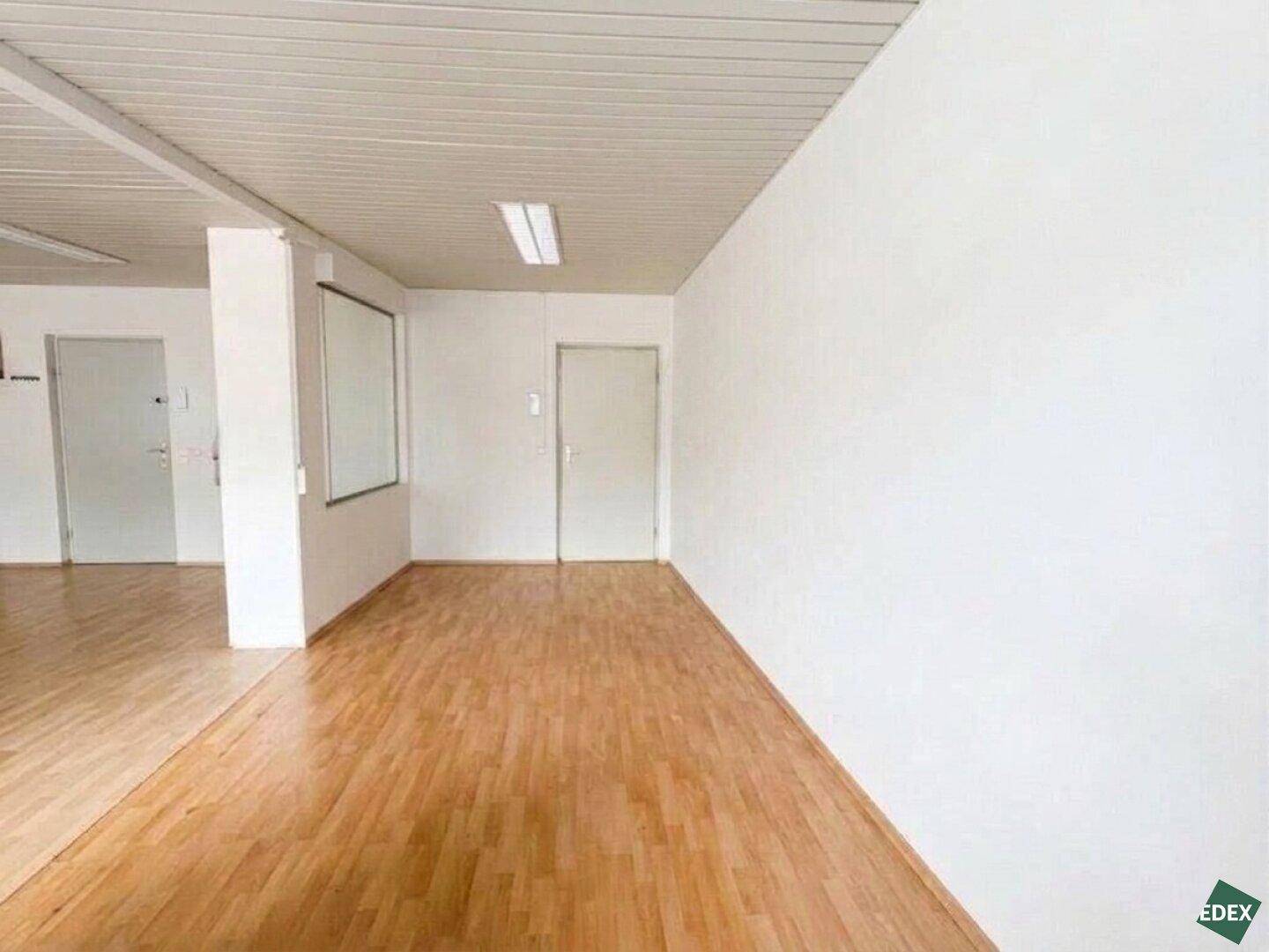 Geräumiger Bürobereich mit hellem Laminatboden, weißen Wänden und mehreren Türen.