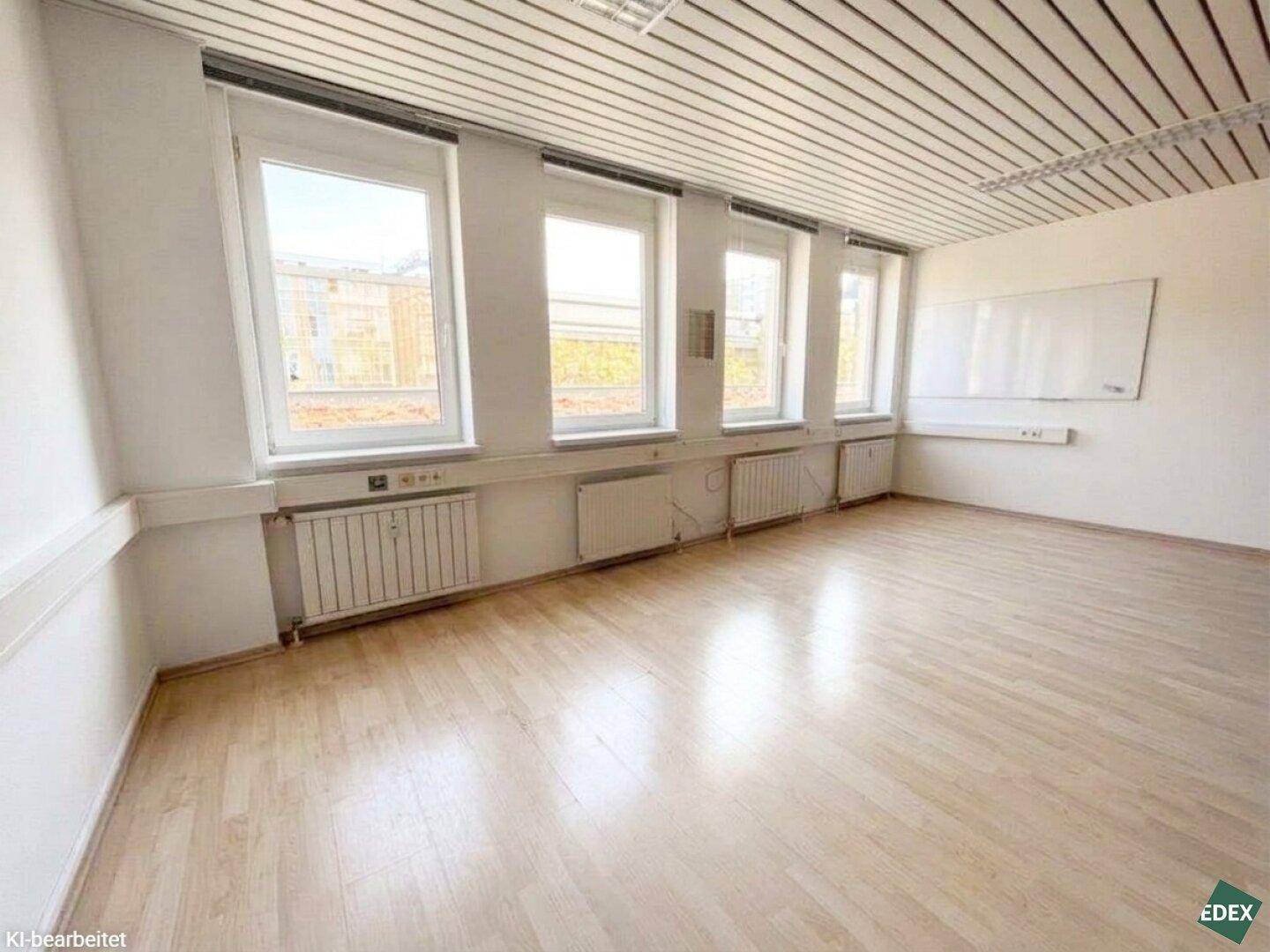 Geräumiger Büroraum mit hellem Holzfußboden, Deckenpaneelen und einer großen Whiteboard-Wand.