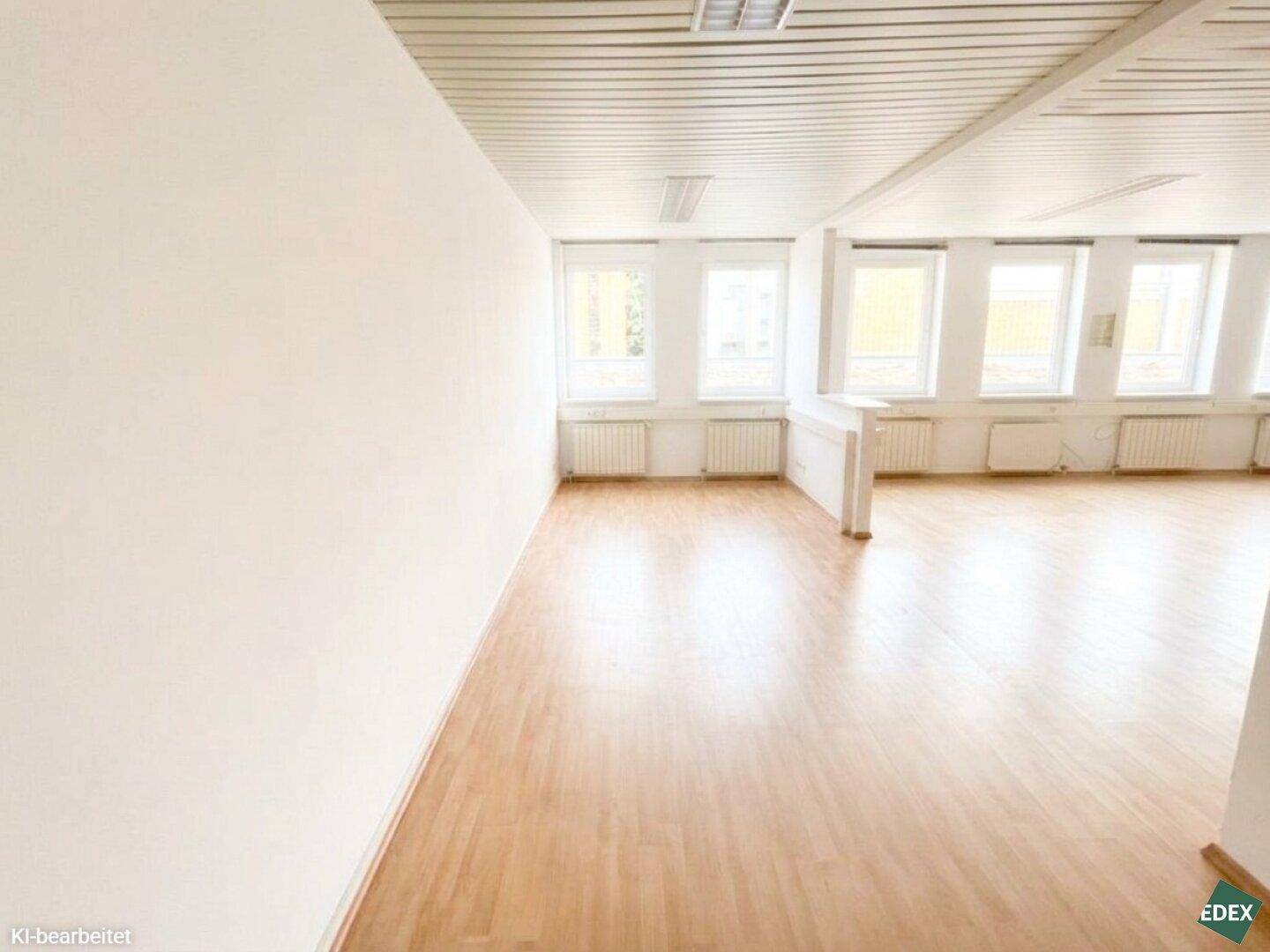 Großer, heller Büroraum mit mehreren Fenstern, Laminatboden und weißer Deckenverkleidung.
