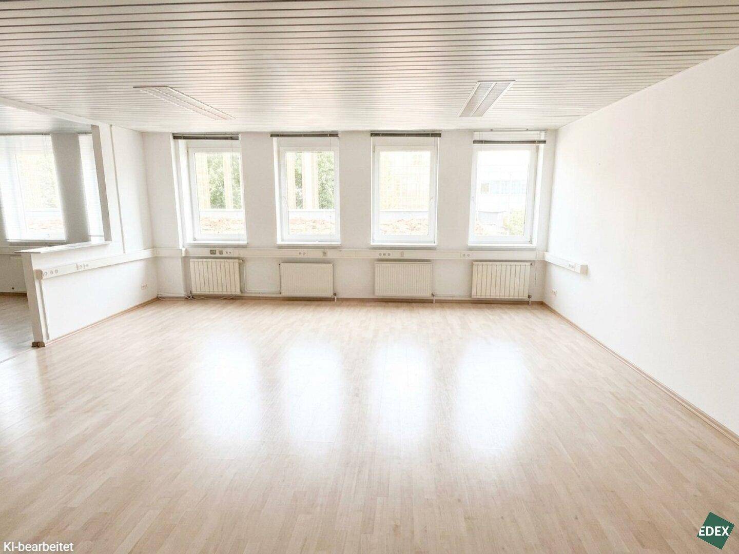 Geräumiger Büroraum mit hellem Holzfußboden, mehreren Fenstern und weiß gestrichenen Wänden, sehr gepflegt.