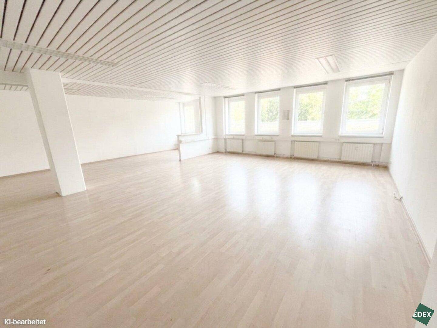 Großer, heller Büroraum mit einer tragenden Säule, Holzfußboden und einer Reihe von Fenstern, in gutem Zustand.