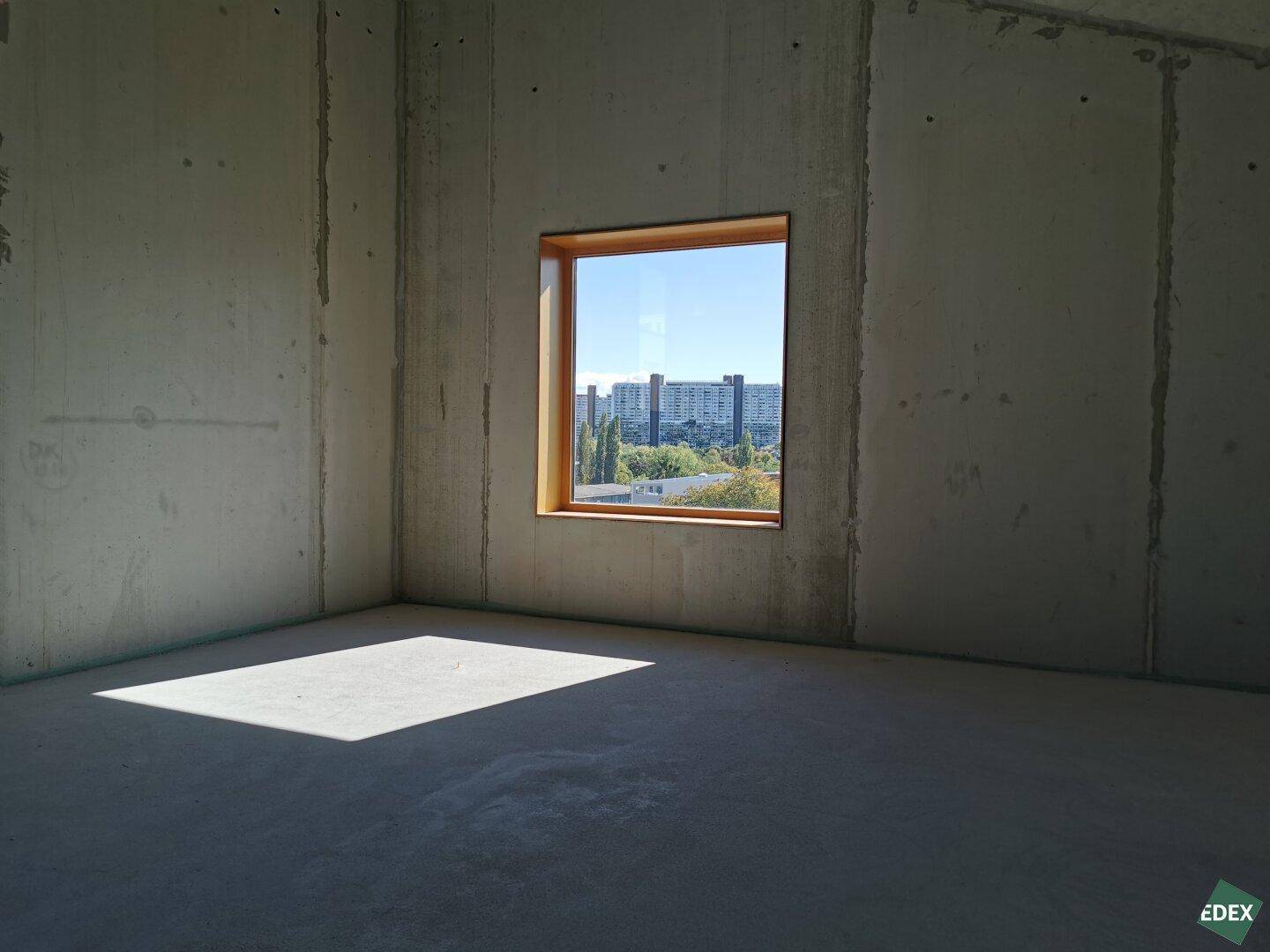 Kleiner Büroraum mit Betonwänden, Betonboden und einem Fenster mit Blick auf die Stadt.