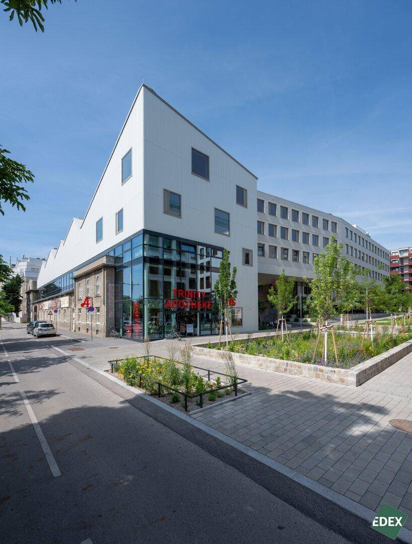 Außenansicht eines modernen Gebäudes mit markanter Architektur, großen Glasflächen und einer Apotheke im Erdgeschoss.
