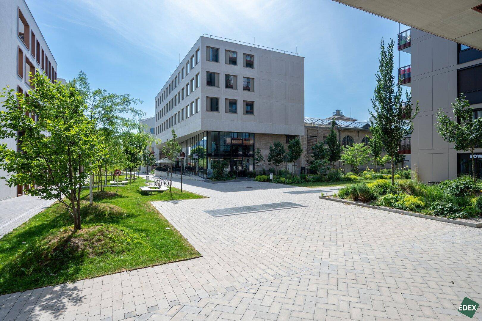 Ansicht eines modernen Bürokomplexes mit gepflegten Grünflächen und Gehwegen unter blauem Himmel.