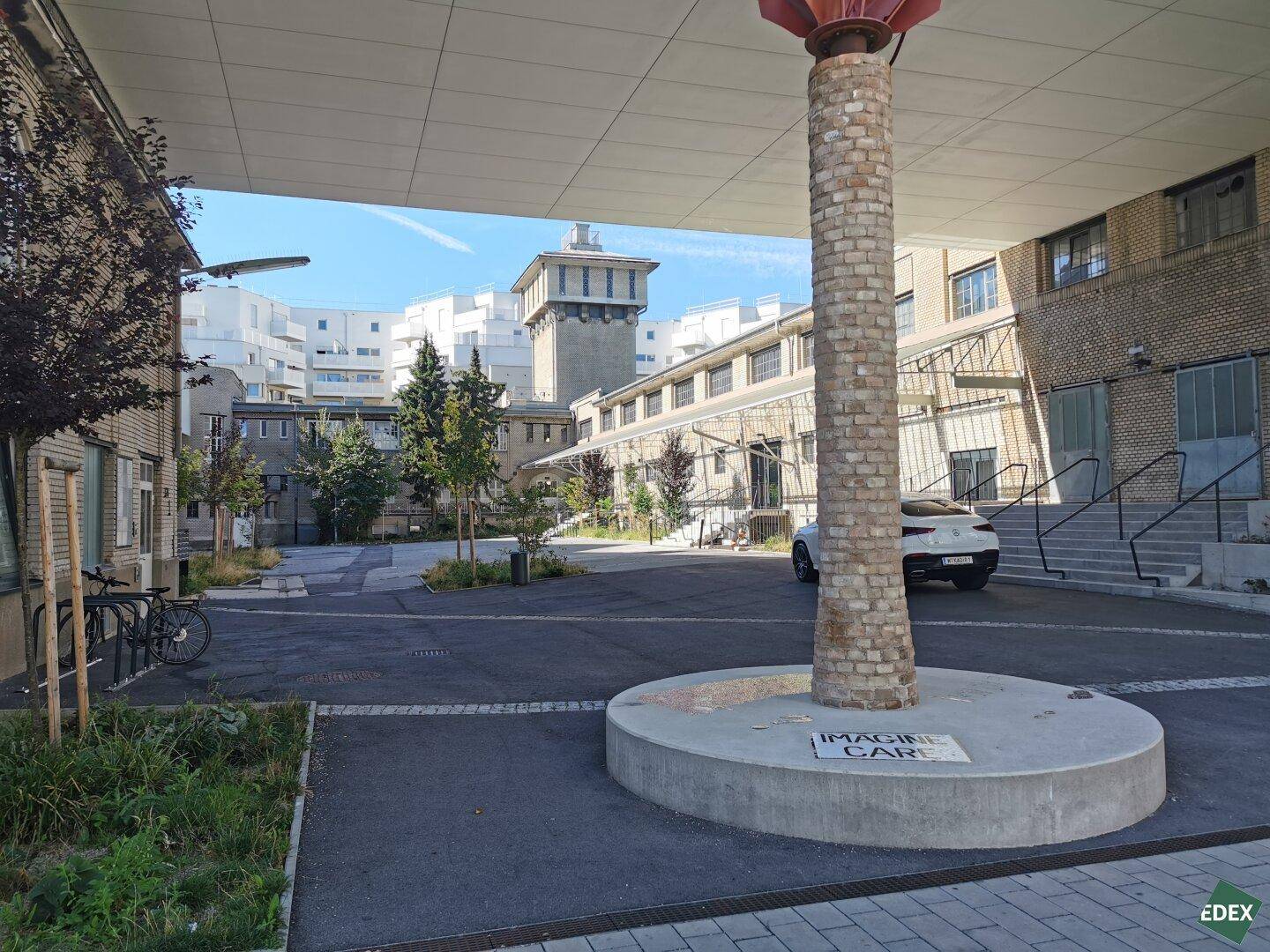 Innenhof mit gepflasterter Fläche, einem markanten Säulenobjekt und umliegenden Gebäuden.