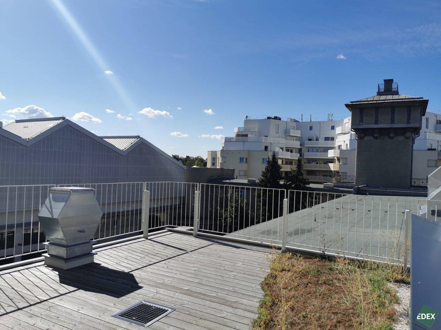 Dachterrasse mit Holzboden und Metallgeländer, bietet einen weiten Blick über die umliegenden Gebäude.