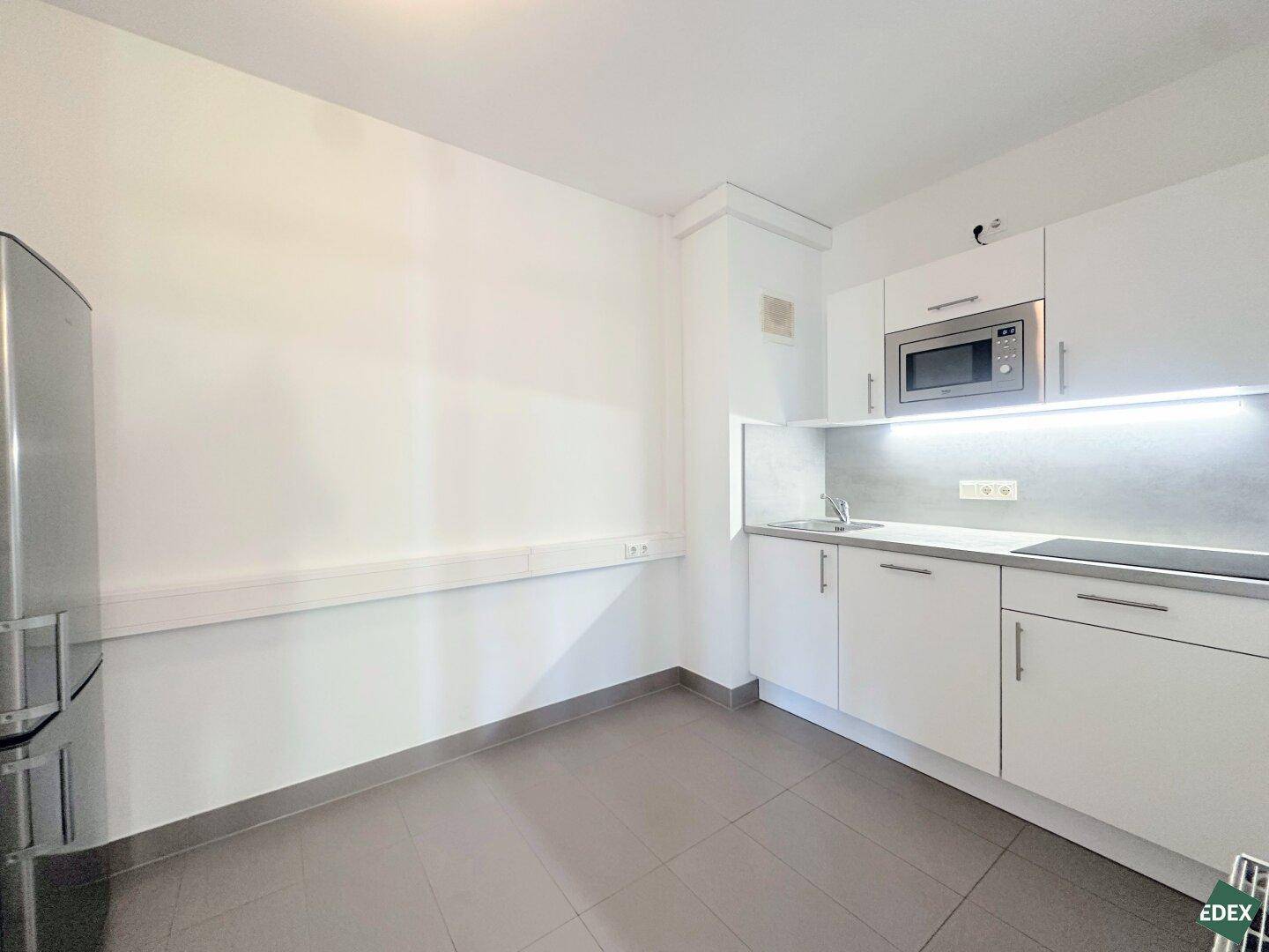 Kleine, moderne Küchenzeile mit weißen Schränken, integrierter Mikrowelle und einem Kühlschrank, ideal für Pausen.