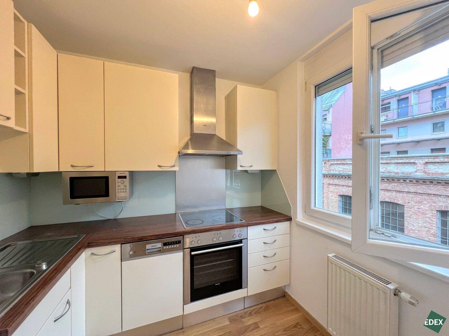 Funktionale Küche mit Einbaugeräten, Dunstabzugshaube und Fenster für natürliches Licht.