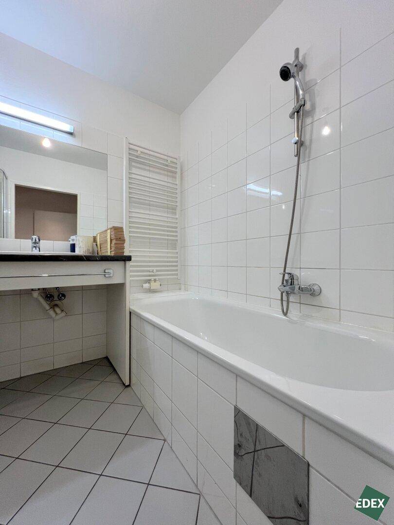 Badezimmer mit Badewanne, weißen Fliesen und einem beheizten Handtuchhalter.