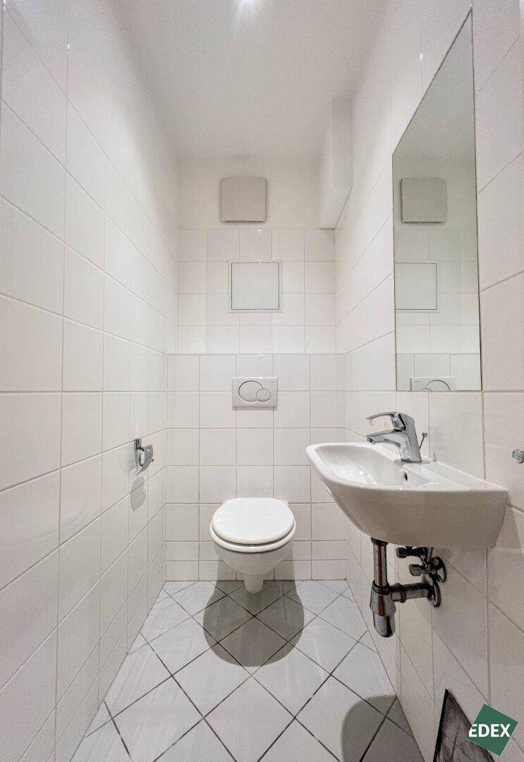 Kleines Gäste-WC mit wandhängender Toilette, Waschbecken und weißen Fliesen.