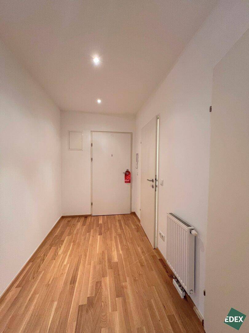 Heller Flur mit Parkettboden und einer Eingangstür, die in die Wohnung führt.