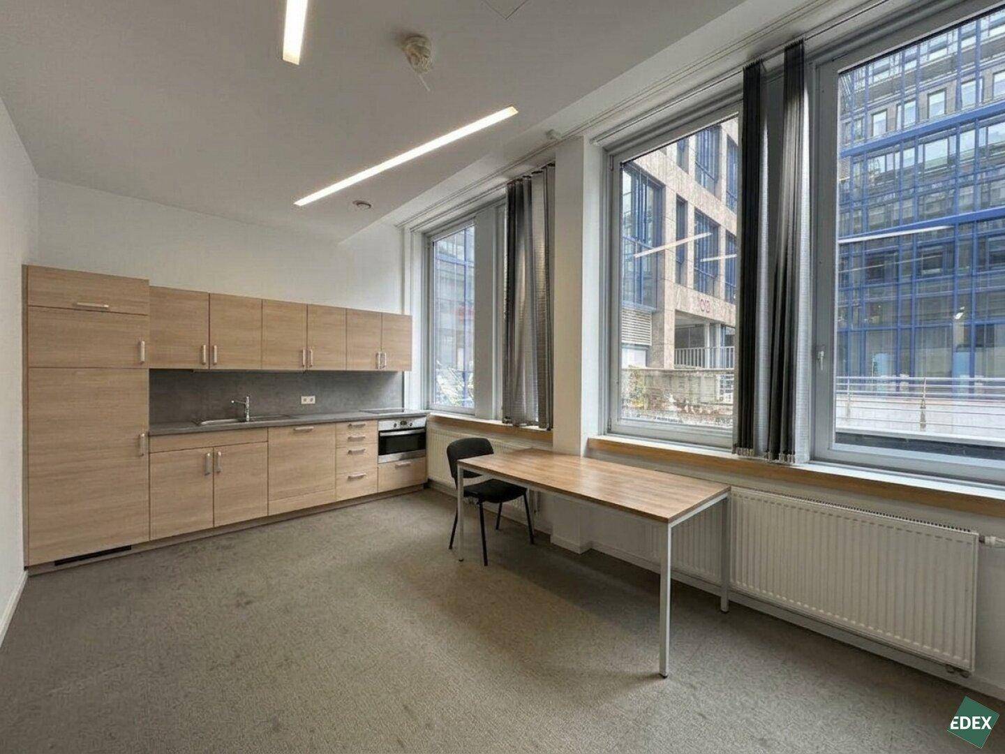 Funktionale Teeküche mit Holzschränken, Spüle, Herd und Blick auf moderne Gebäude.