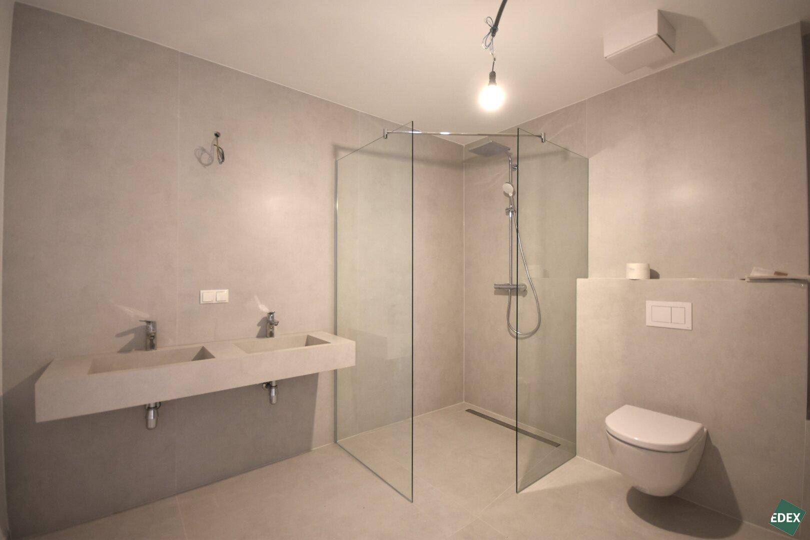 Modernes Badezimmer mit Doppelwaschbecken, begehbarer Dusche und Wand-WC.