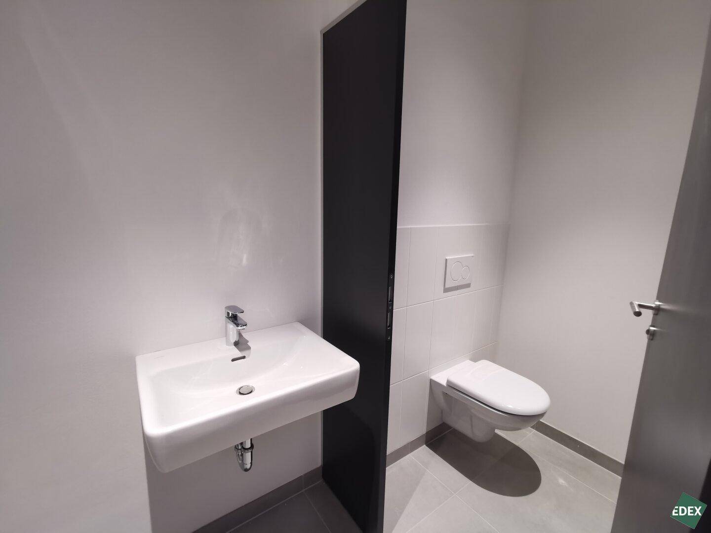 Modernes Badezimmer mit wandhängendem WC, rechteckigem Waschbecken und grauen Fliesen.