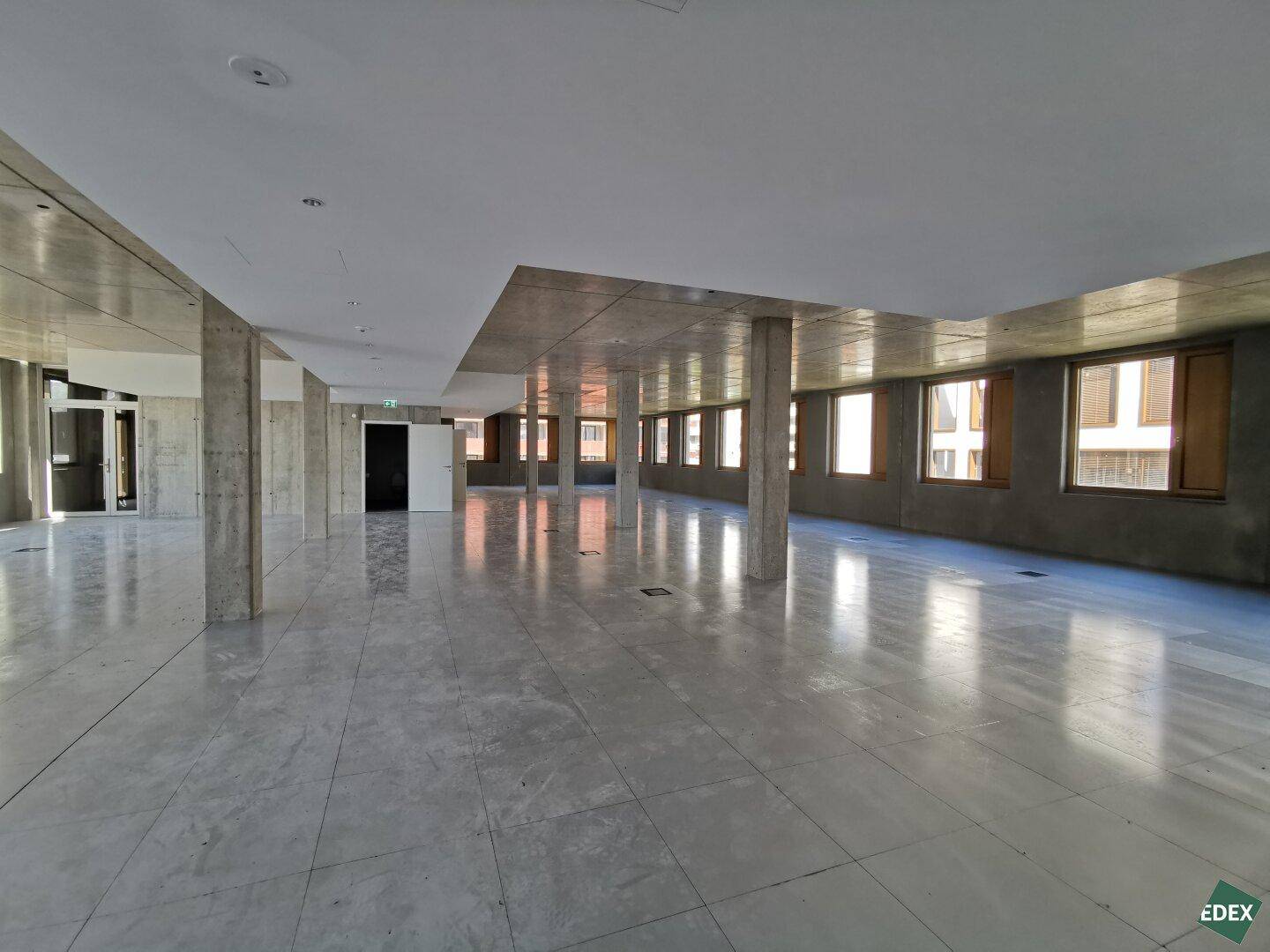 Geräumiger Bürobereich mit offenem Grundriss, Betonstützen und Zugang zu weiteren Räumen.