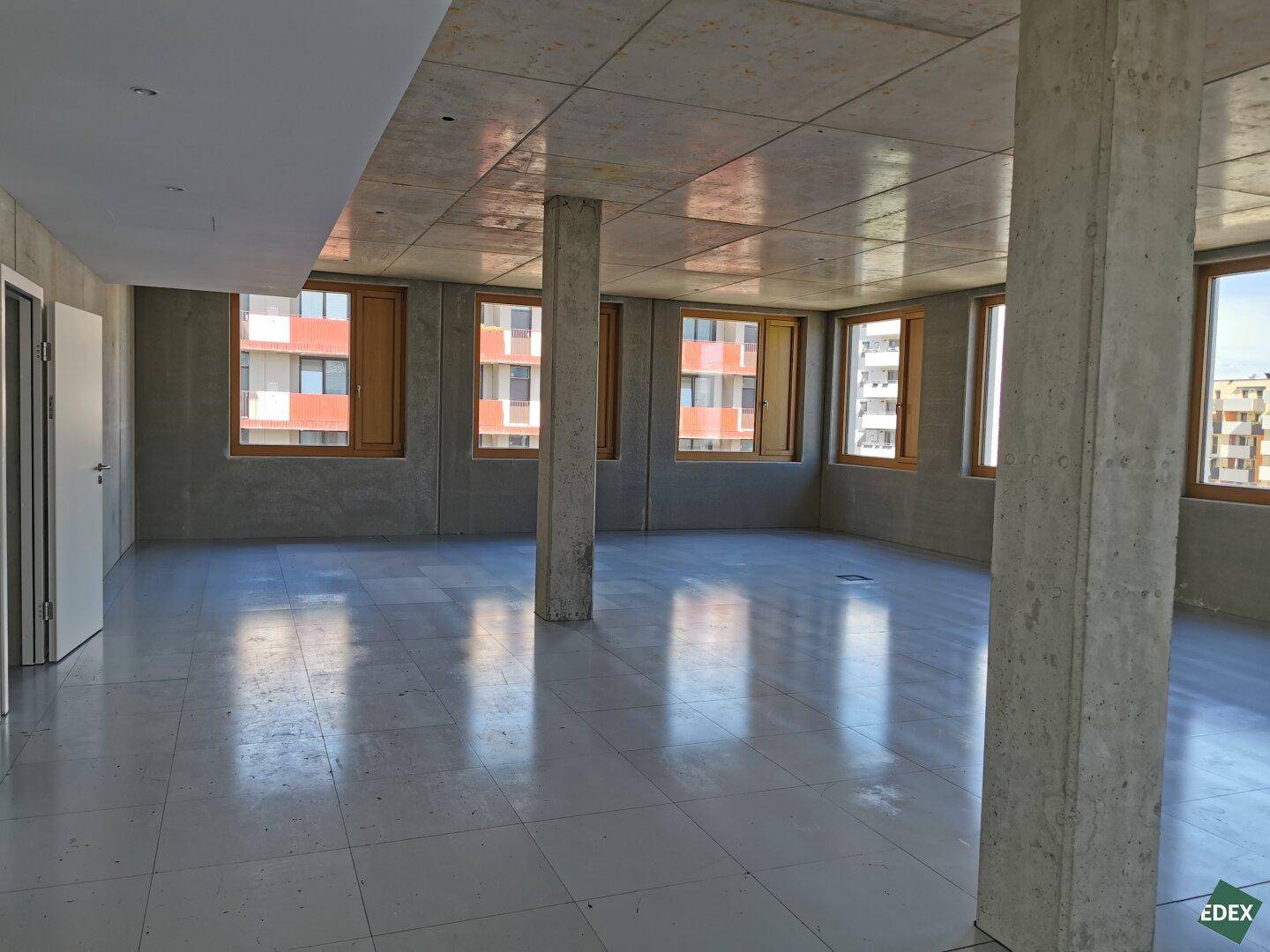 Heller Büroraum mit Blick auf umliegende Gebäude und viel Tageslicht durch die großen Fenster.