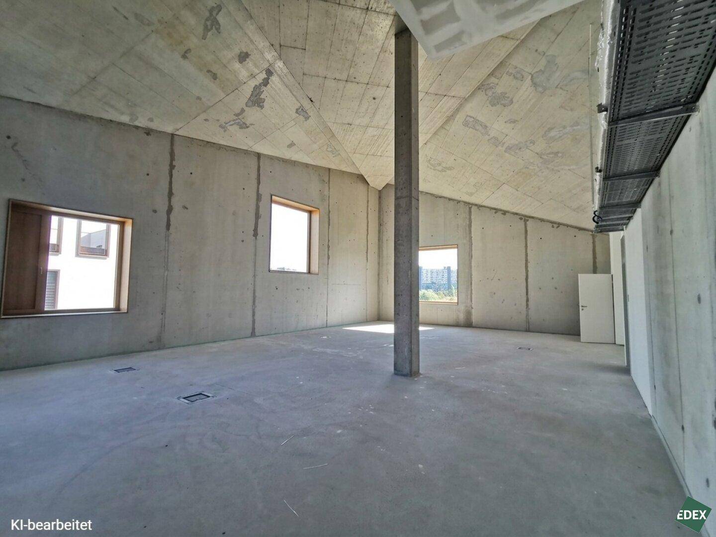 Großer, unfertiger Raum mit schräger Betondecke und zentraler Säule, ideal für flexible Nutzung.