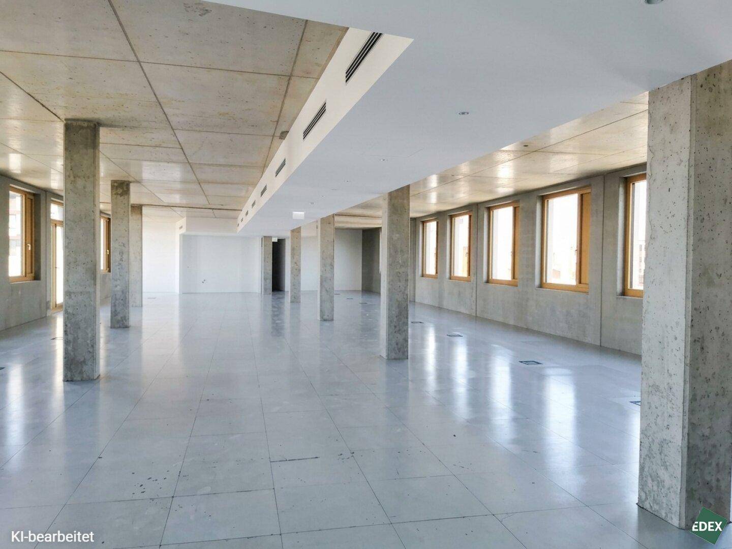 Weitläufiger, heller Bürobereich mit zahlreichen Fenstern, Betonsäulen und einem modernen Fliesenboden.