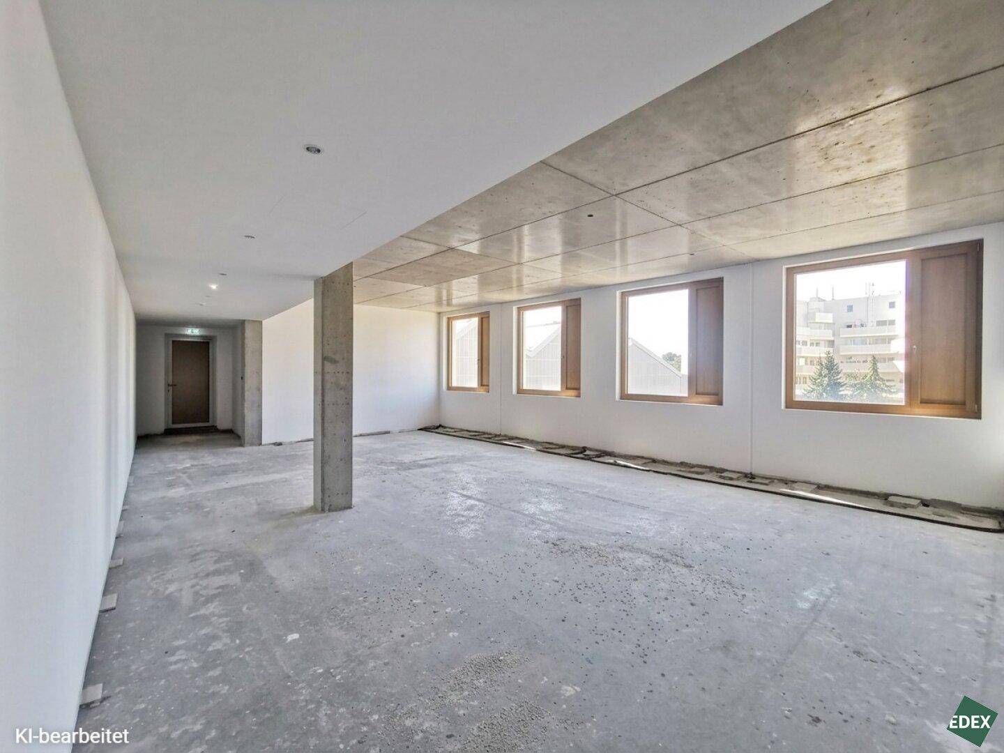 Großer, leerer Raum in einem Neubau mit Betonboden und mehreren Fenstern, bereit für den Ausbau.