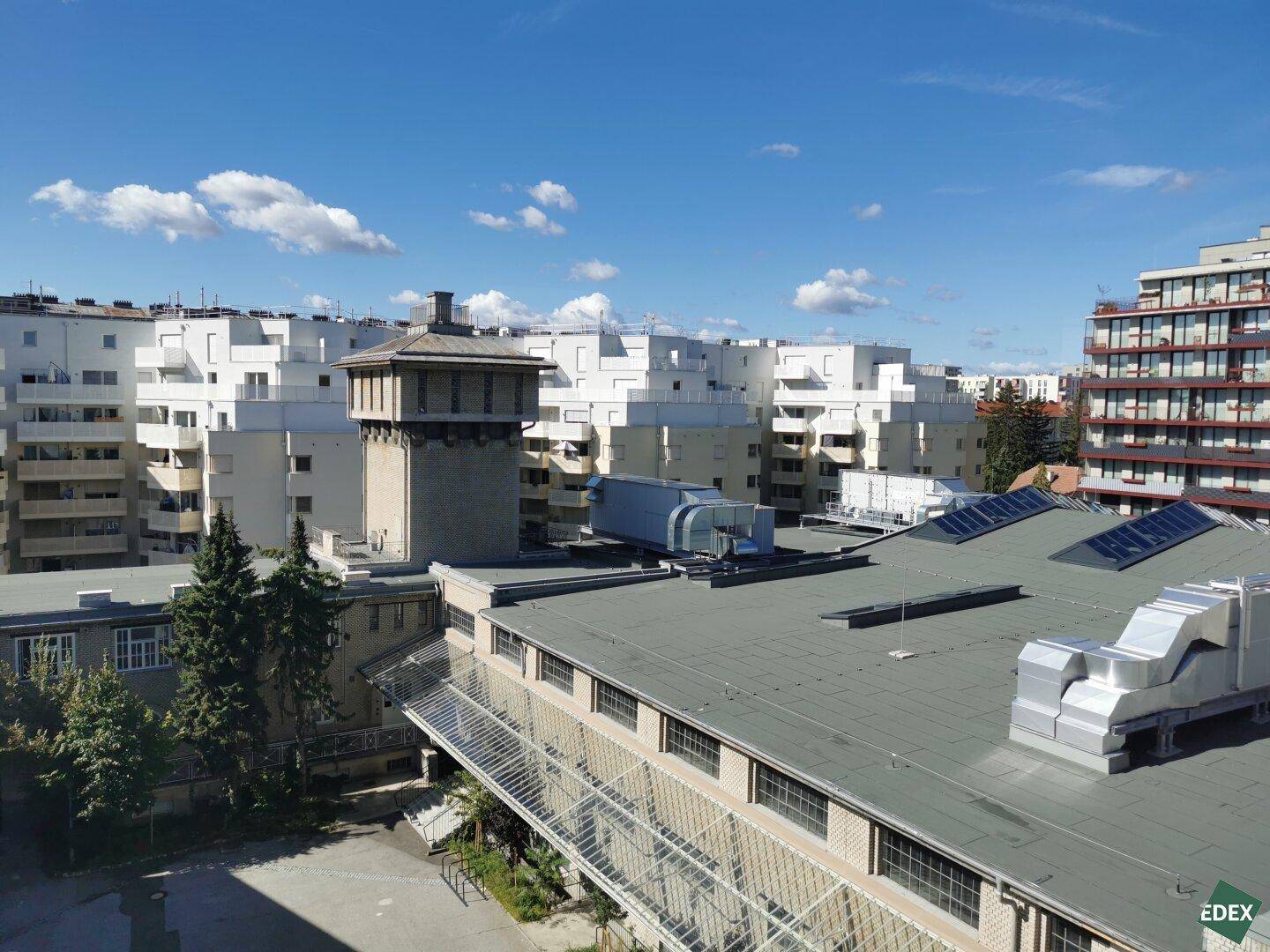Panoramablick über eine städtische Bebauung mit verschiedenen Gebäudetypen und Dächern unter blauem Himmel.
