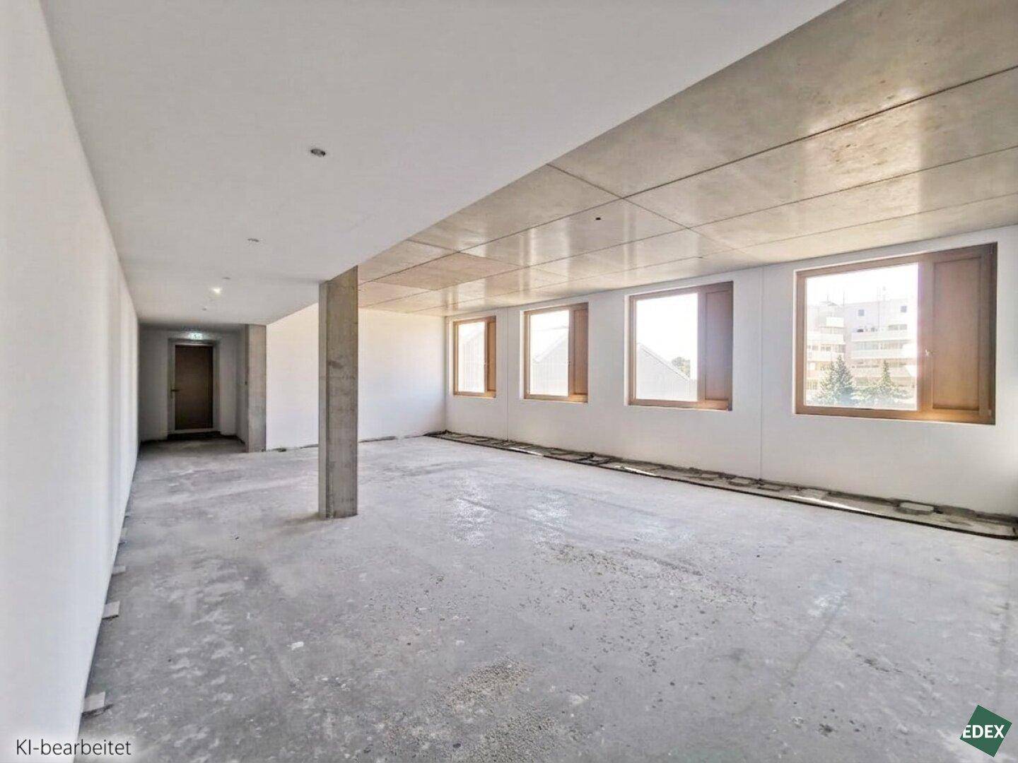 Spacious, unfinished room with concrete ceiling, white walls, and a row of windows providing ample natural light.