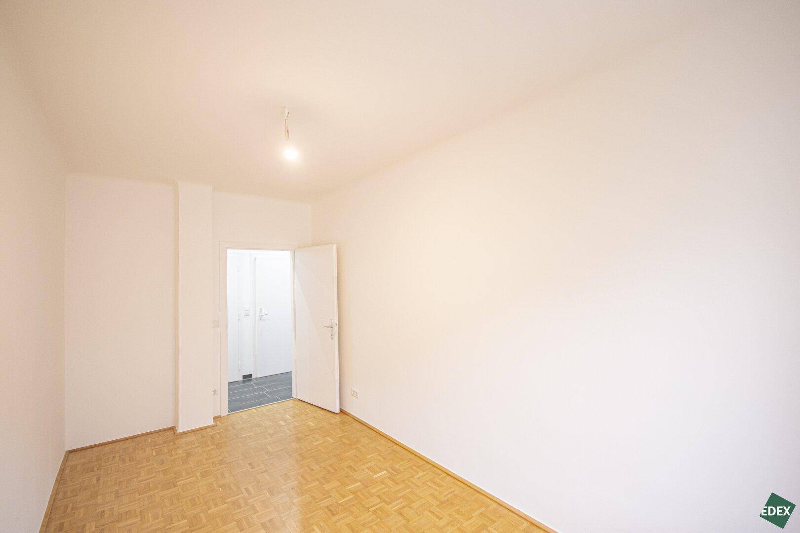 Leeres Zimmer mit Parkettboden und weiß gestrichenen Wänden, bereit zur individuellen Gestaltung.