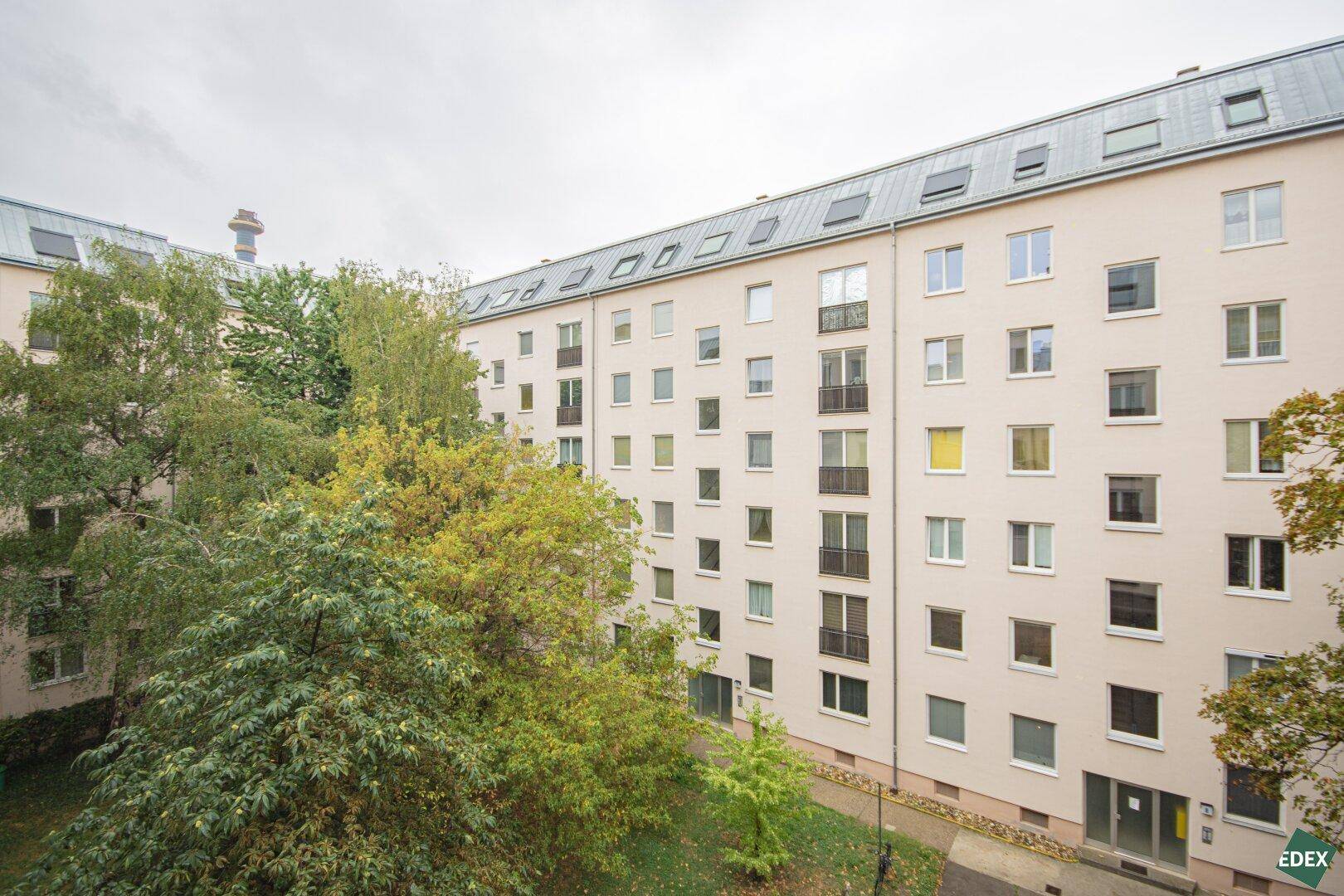 Mehrstöckiges Wohngebäude mit zahlreichen Fenstern und Balkonen, umgeben von Bäumen.