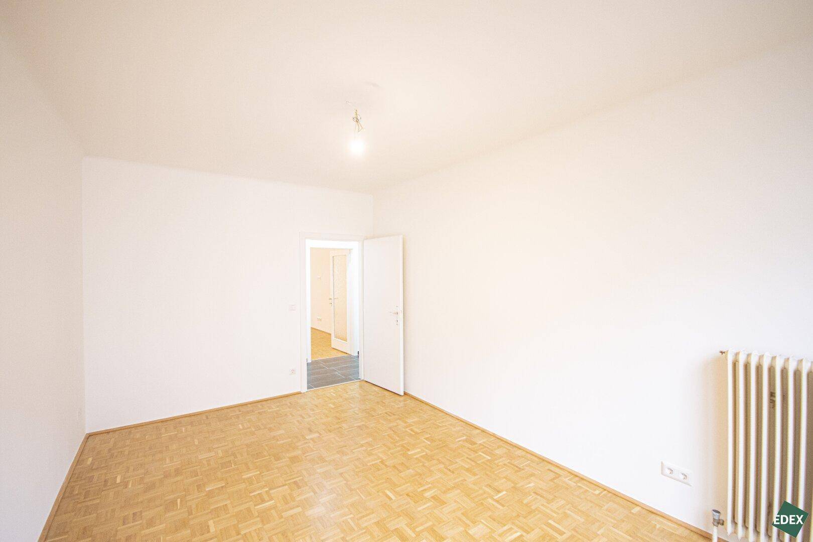 Helles Zimmer mit Parkettboden und Zugang zu einem weiteren Raum, ideal als Schlafzimmer.