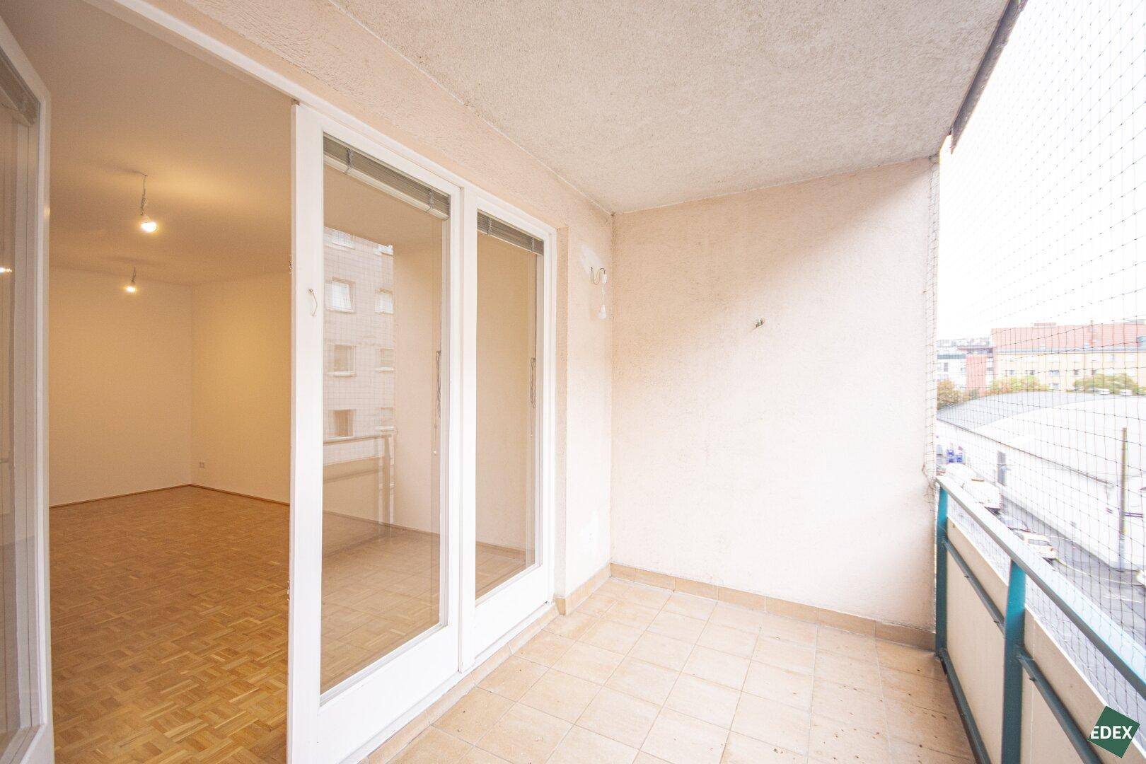 Balkon mit Fliesenboden und Zugang zu einem hellen Innenraum mit Parkett.