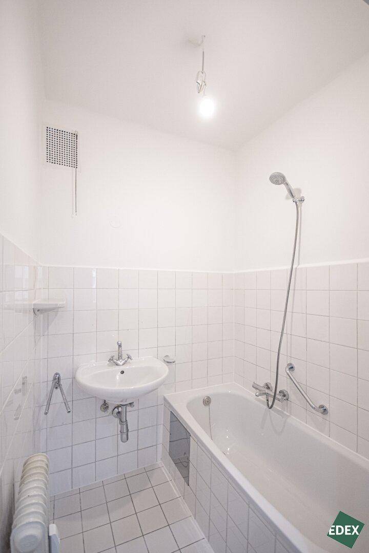Helles Badezimmer mit Badewanne, Waschbecken und weißen Fliesen, funktional und sauber.