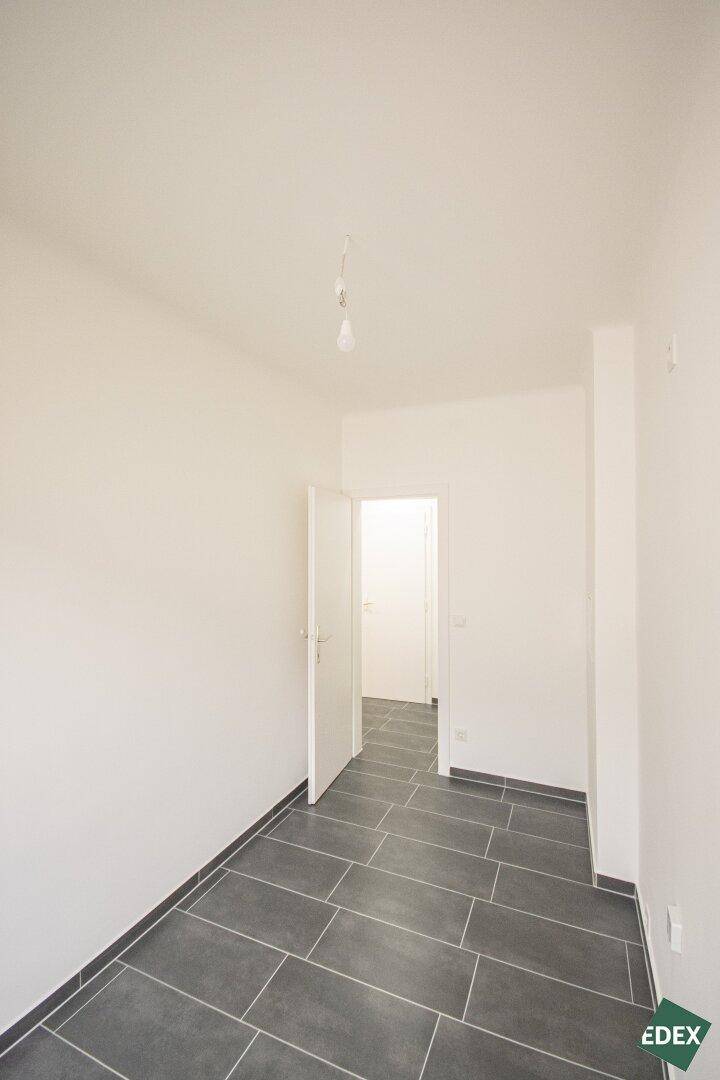Heller Flur mit dunklen Fliesen und weiß gestrichenen Wänden, der zu weiteren Räumen führt.