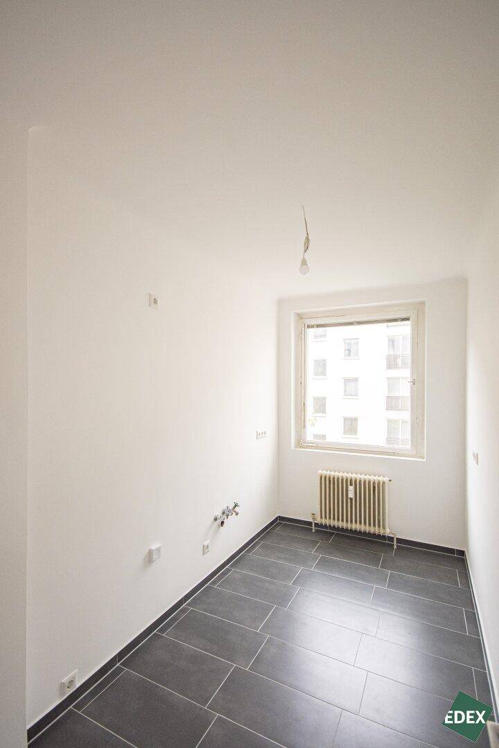 Leerer Raum, vorbereitet für eine Küche, mit dunklen Fliesen und einem Fenster.