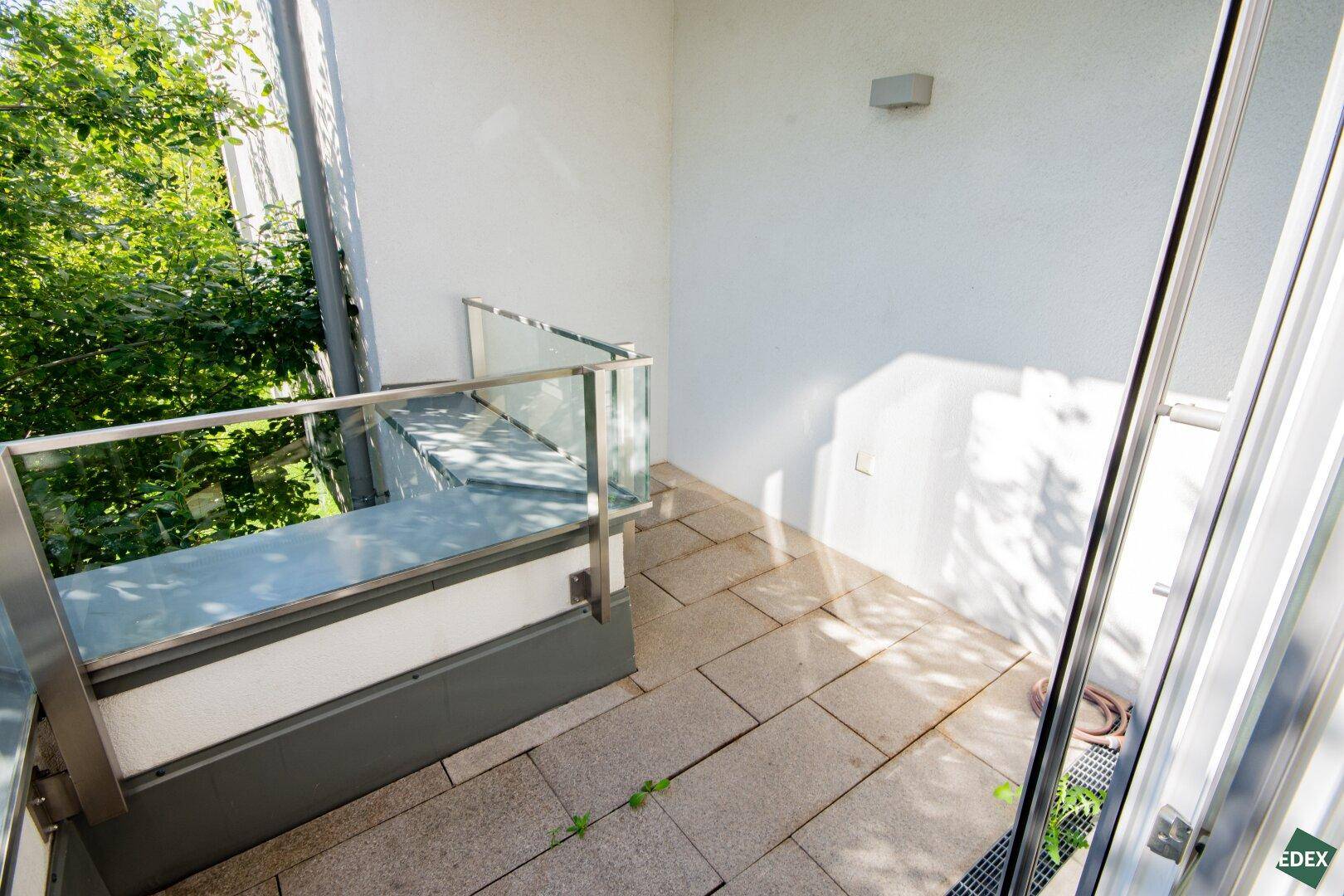Heller Balkon mit Fliesenboden und Glasgeländer, ideal für entspannte Stunden im Freien mit Blick ins Grüne.