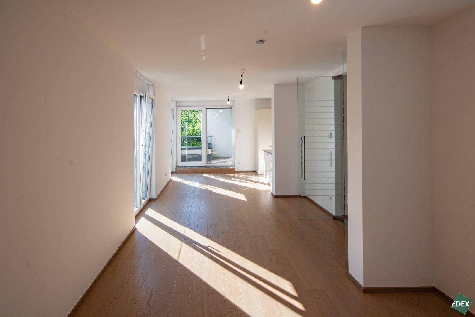 Geräumiger Wohnbereich mit Holzboden, viel Tageslicht und Zugang zu einem Balkon, offen gestaltet.