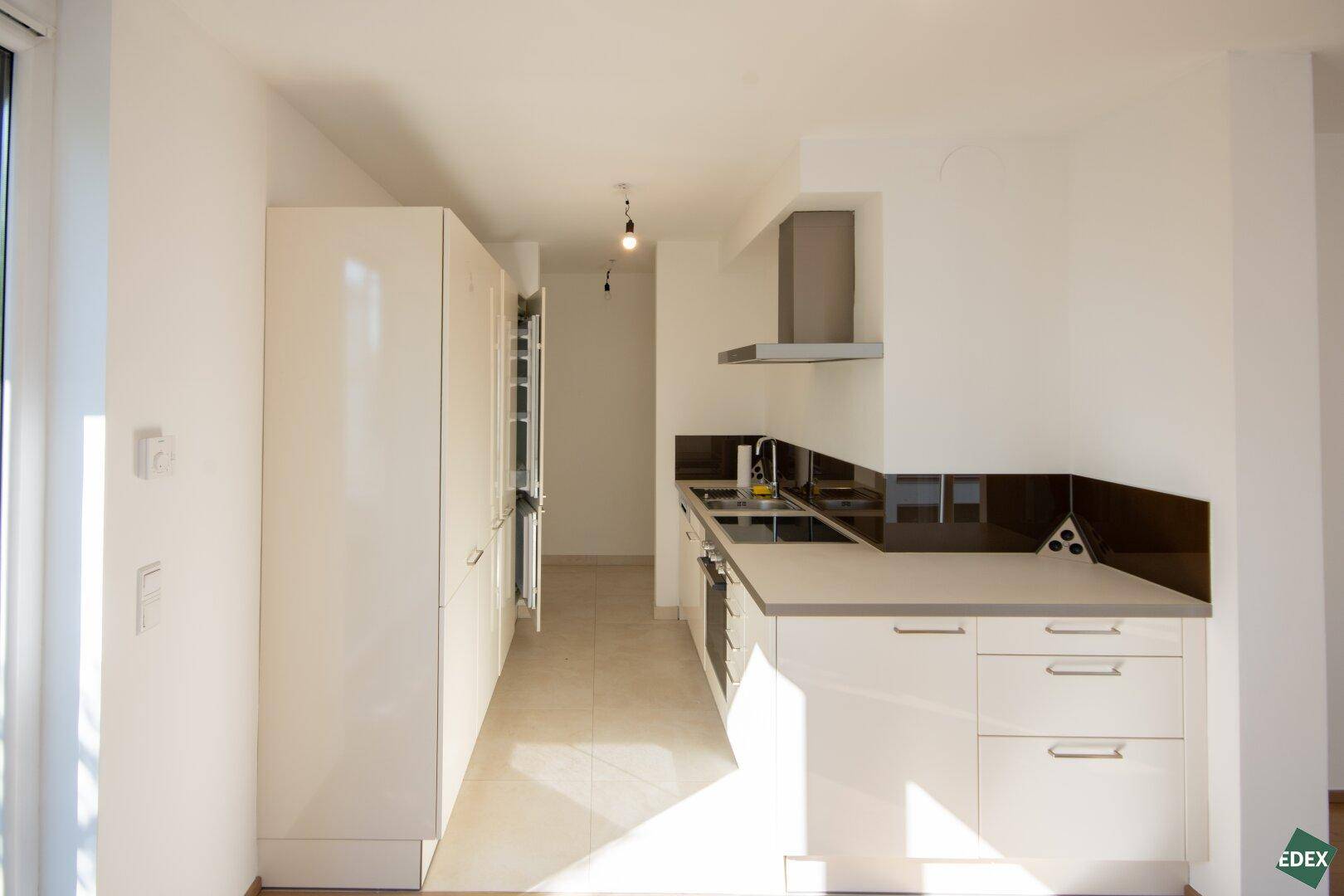 Moderne Einbauküche mit weißen Hochglanzfronten, integrierten Geräten und Dunstabzugshaube.