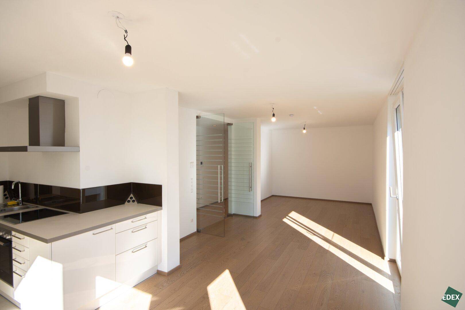 Offener Wohn- und Essbereich mit integrierter Küche und hellem Holzboden, ideal für geselliges Beisammensein.