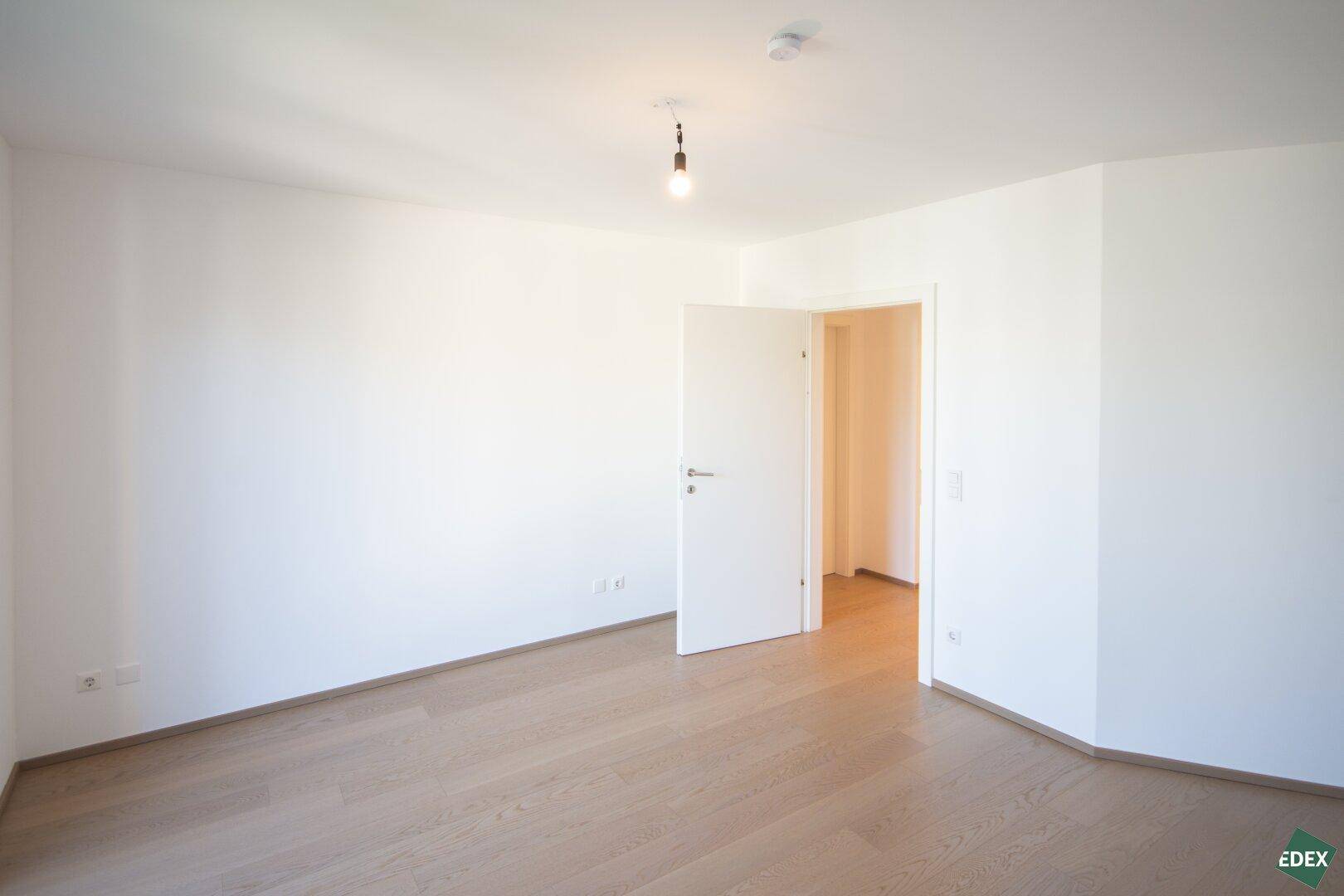 Leeres Zimmer mit hellem Holzboden und weiß gestrichenen Wänden, bereit zur individuellen Gestaltung.