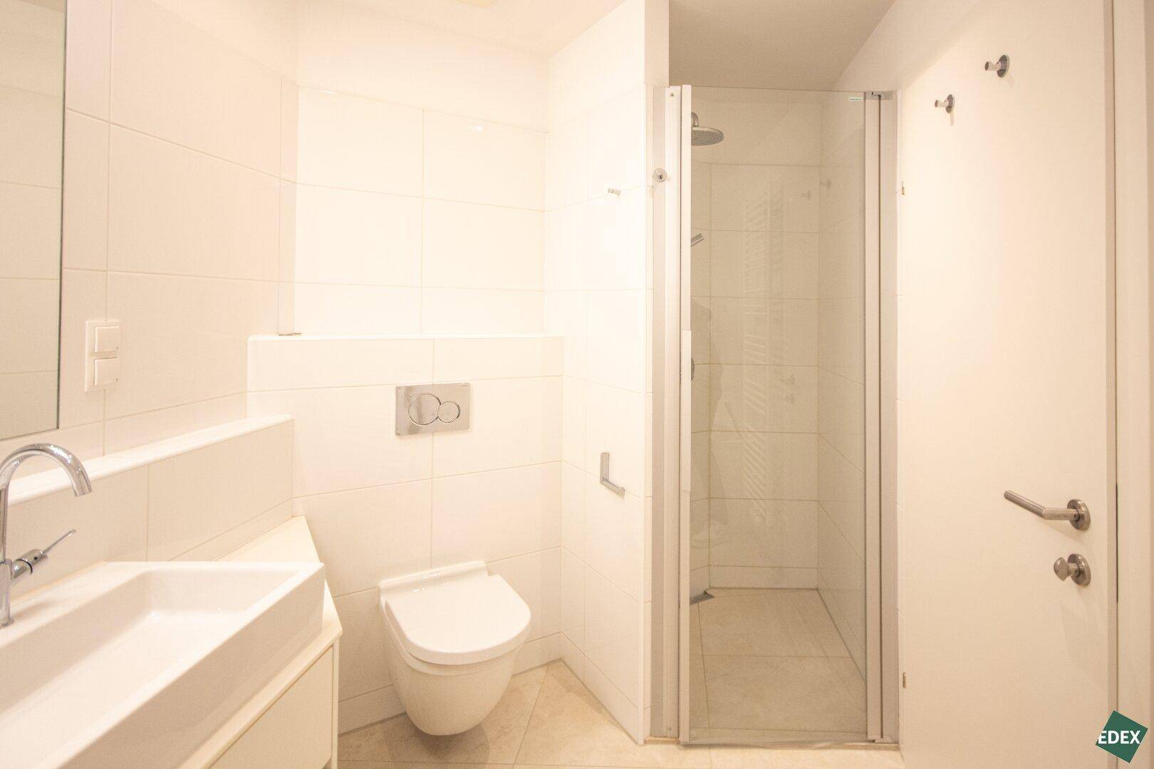Modernes Badezimmer mit Duschkabine, wandhängendem WC und hellem Fliesenboden, funktional und stilvoll.