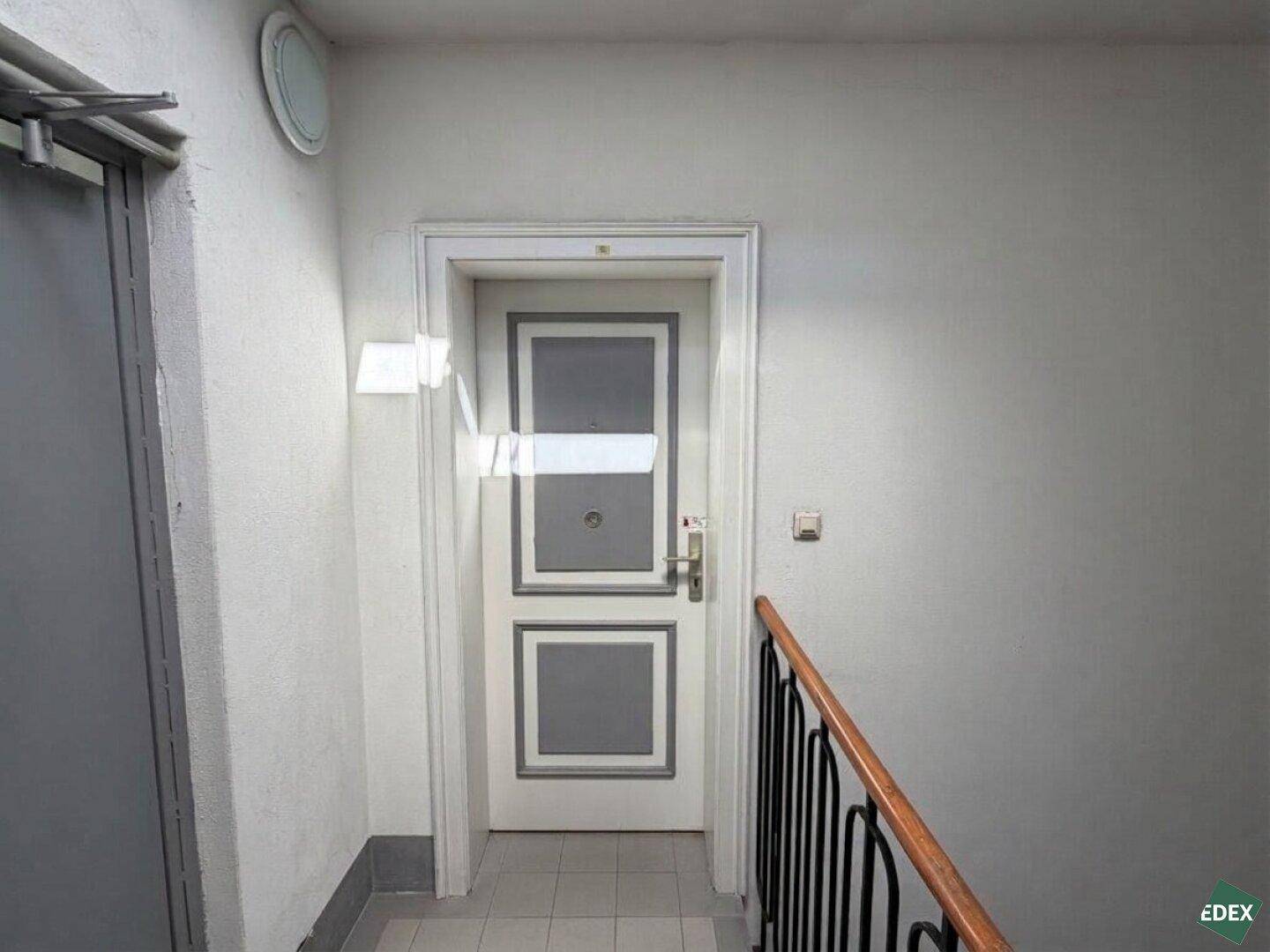 Eingangstür einer Wohnung im Gemeinschaftsflur mit dekorativem weiß-grauem Paneeldesign.