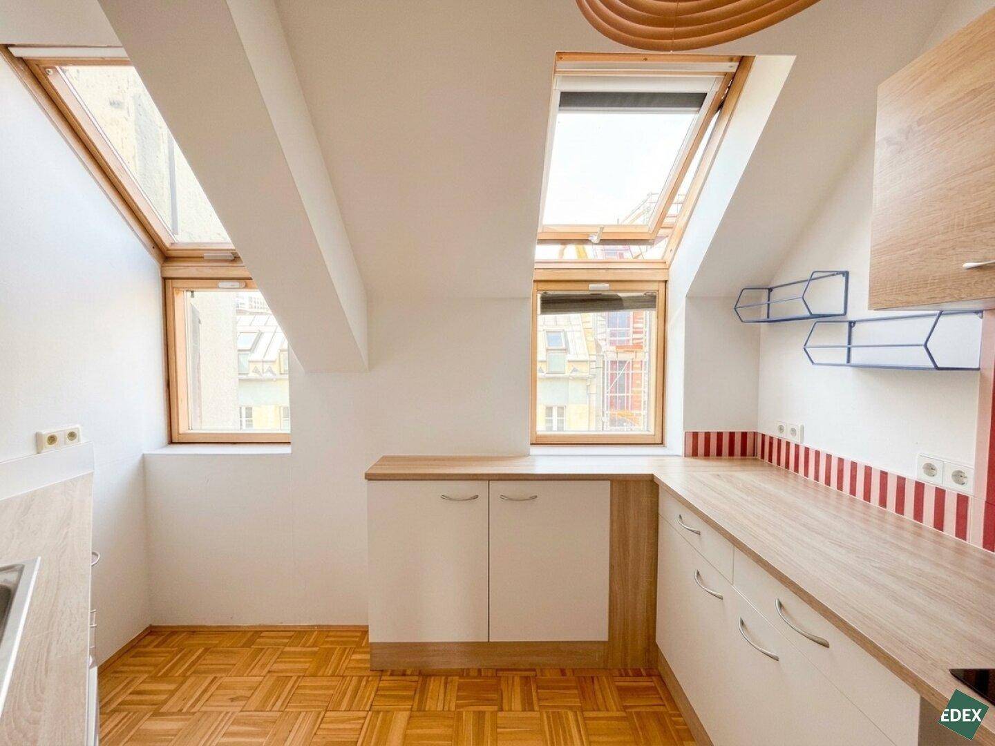 Helle Küche im Dachgeschoss mit weißen Schränken, Holz-Arbeitsplatten und roten Streifenfliesen als Rückwand.