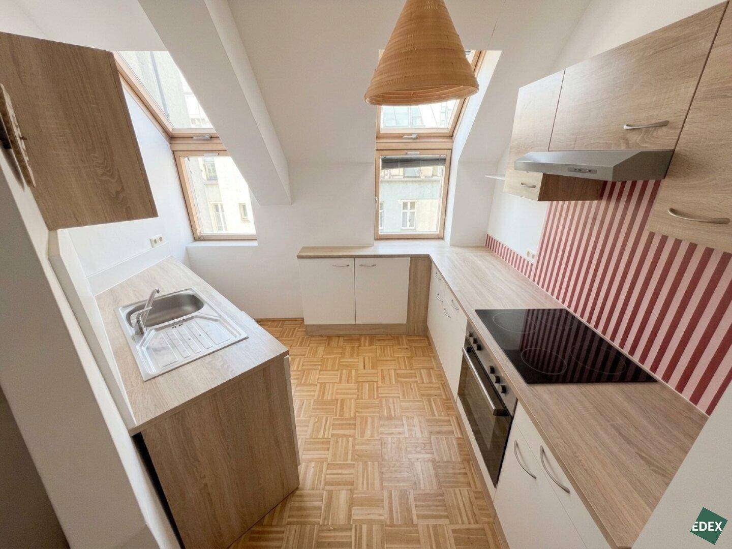 Funktionale Küche mit Spüle, Induktionskochfeld und Backofen unter Dachfenstern im Dachgeschoss.