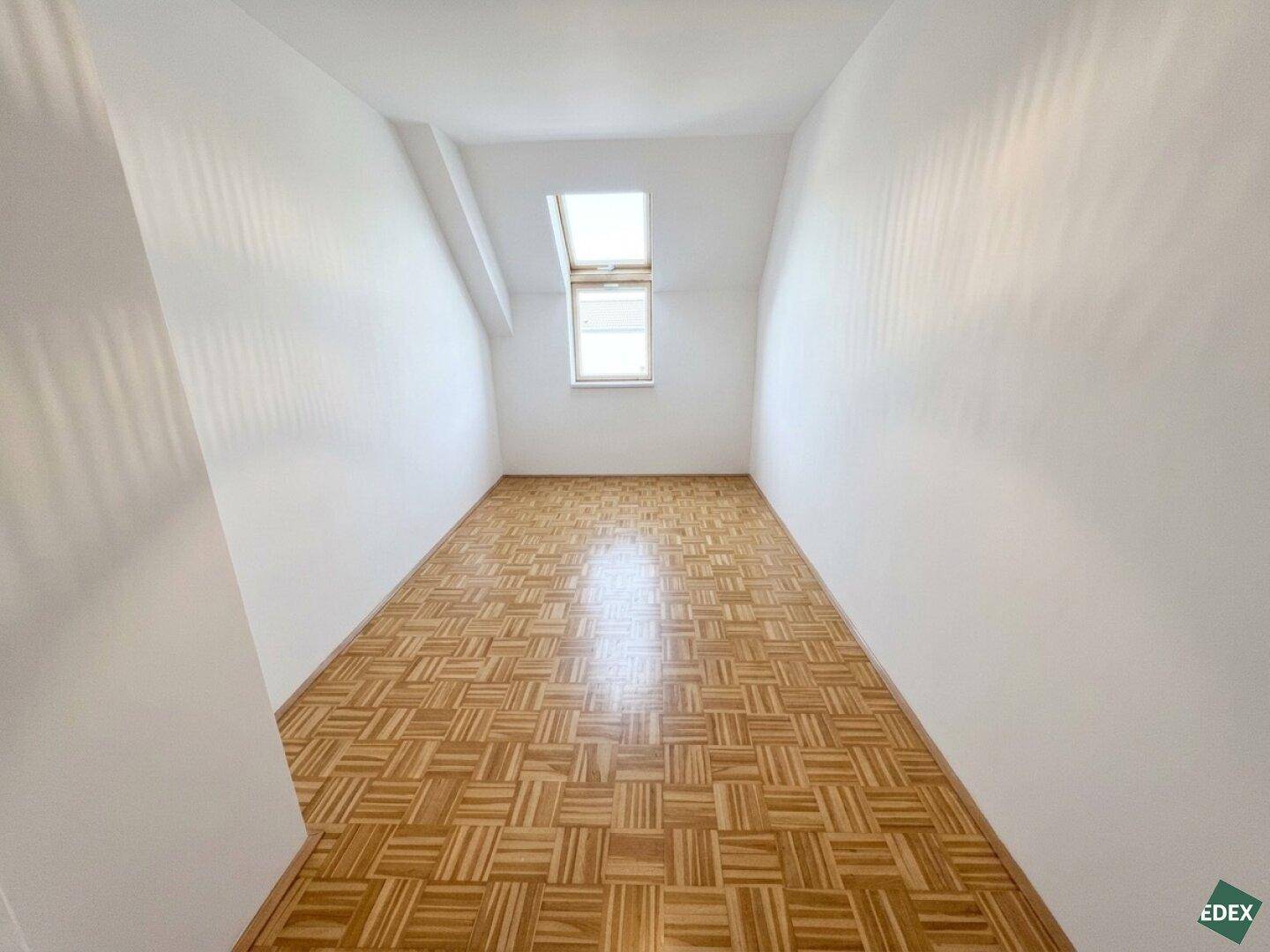 Schmaler Raum im Dachgeschoss mit Parkettboden und einem Dachfenster, geeignet als Schlafzimmer oder Büro.